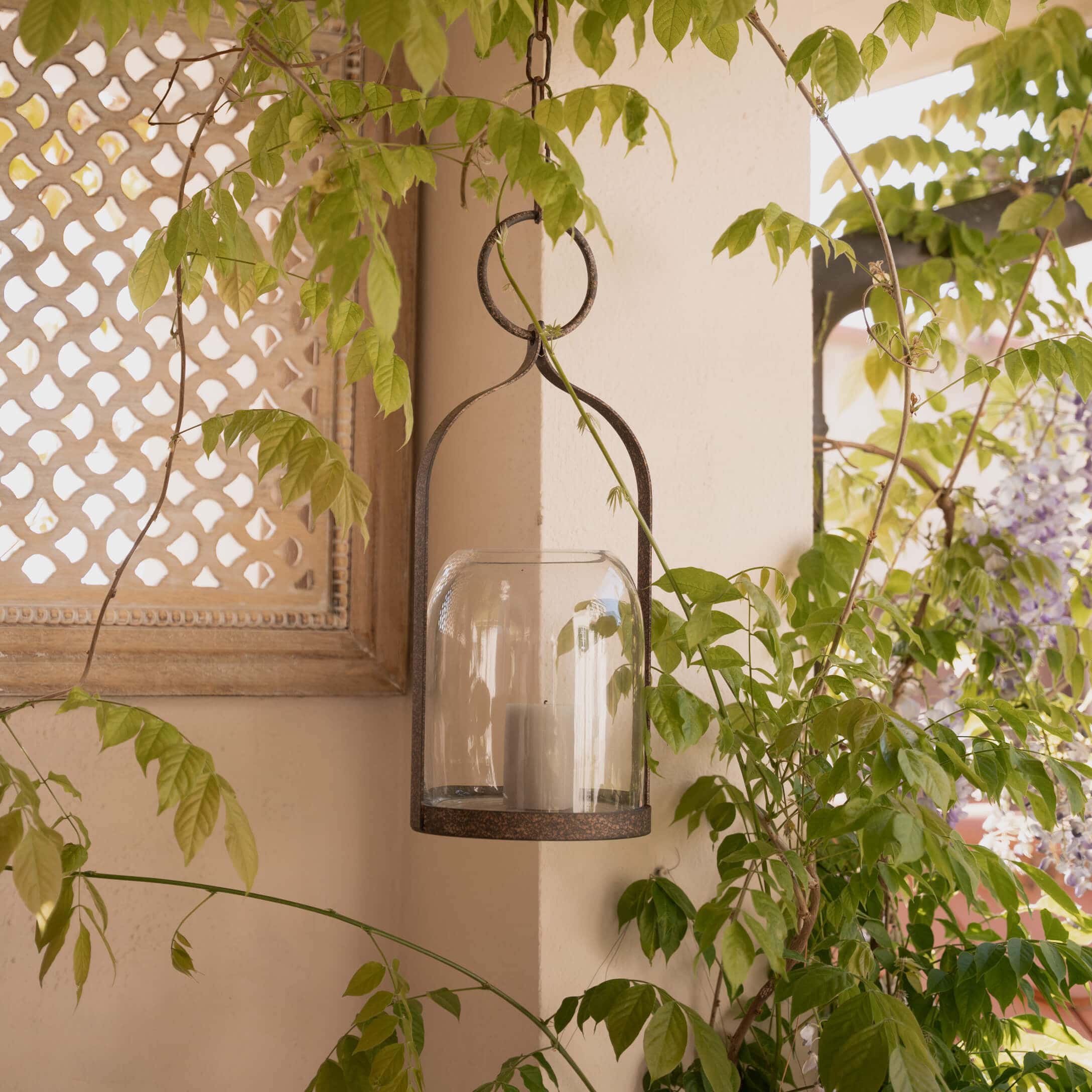Hangende lantaarn van metaal en glas met witte kaars, rustieke tuindecoratie