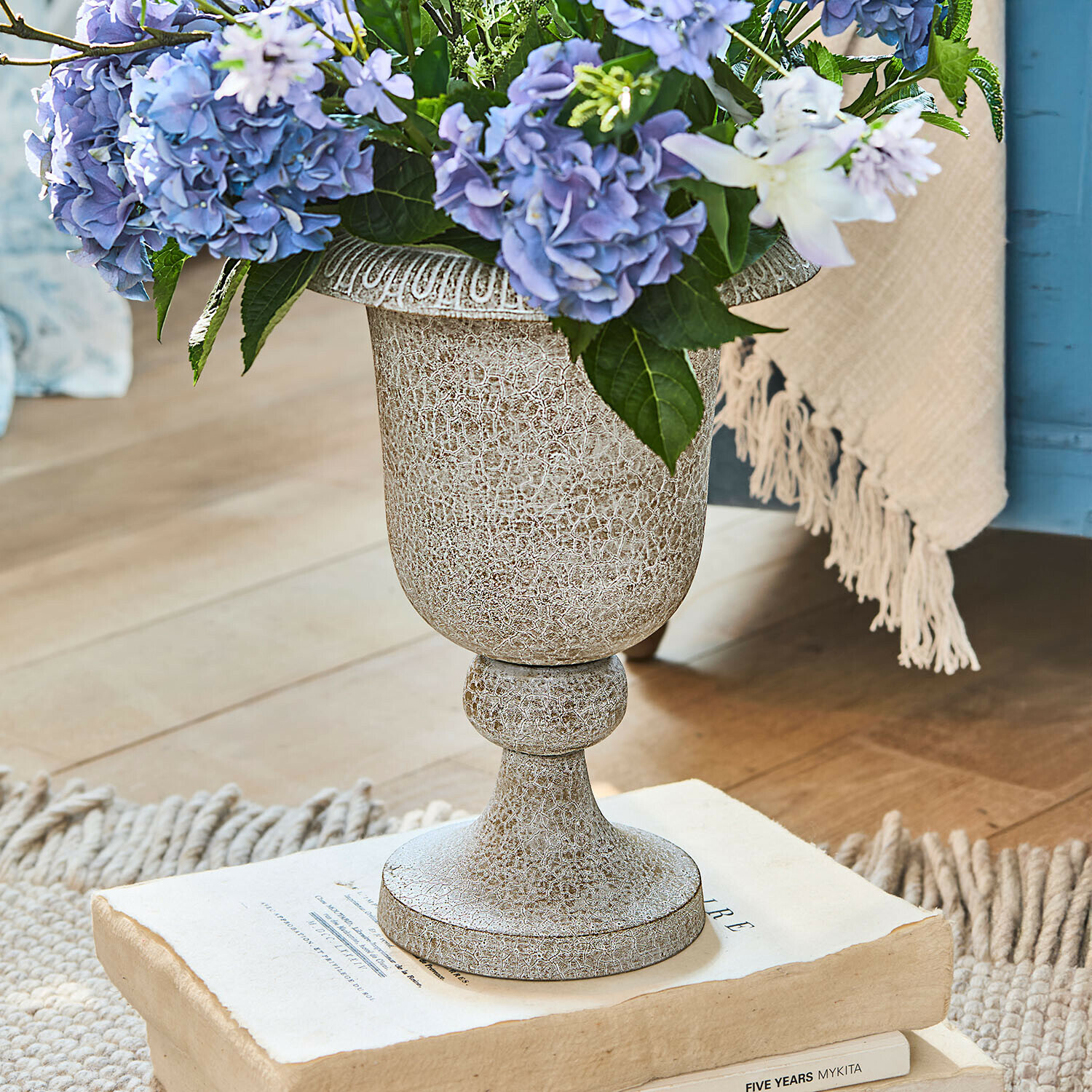 Decoratieve beige keramische vaas met patina en blauwe bloemen op oude boeken geplaatst