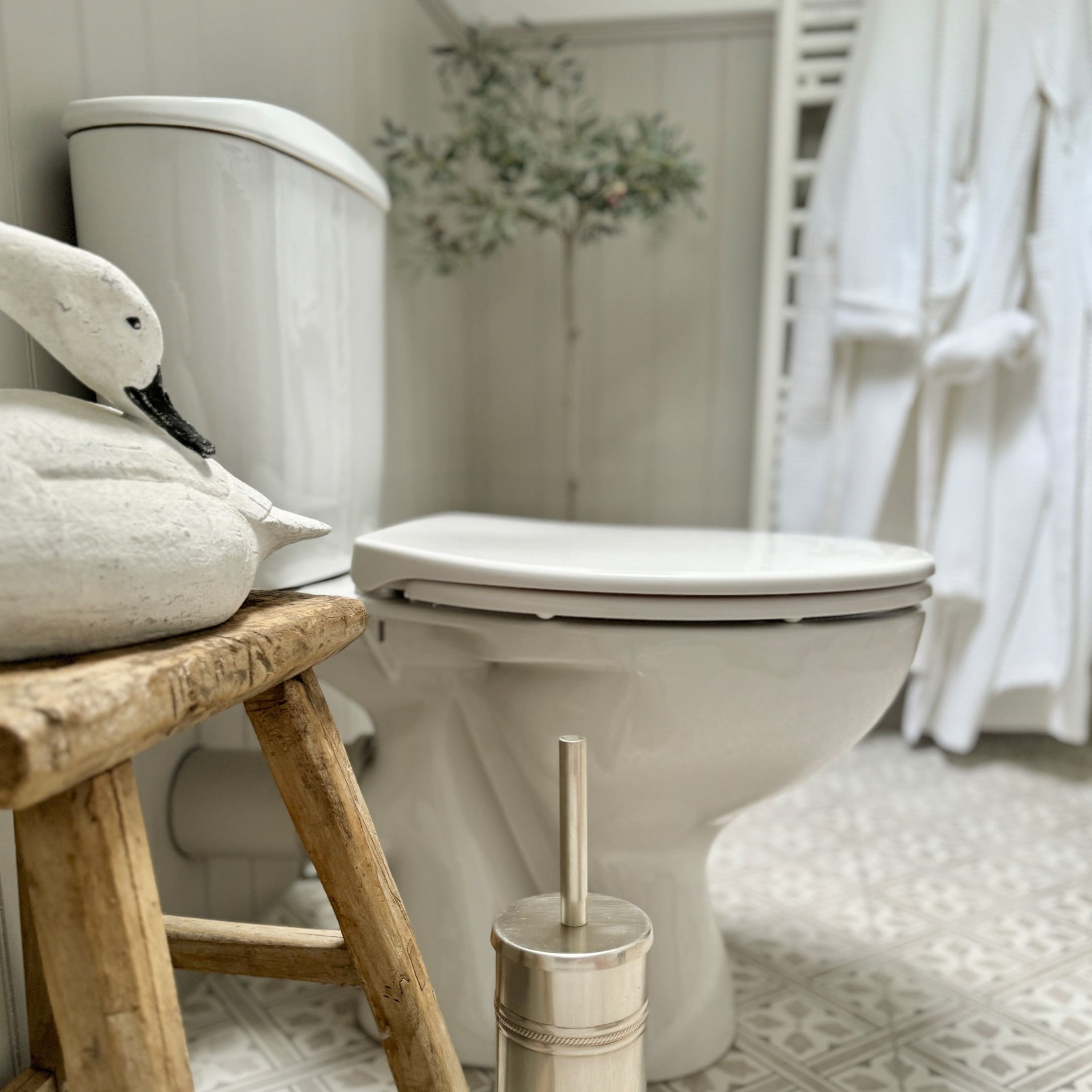 Witte keramische toilet in badkamer met houten kruk en rustieke zwanendecoratie