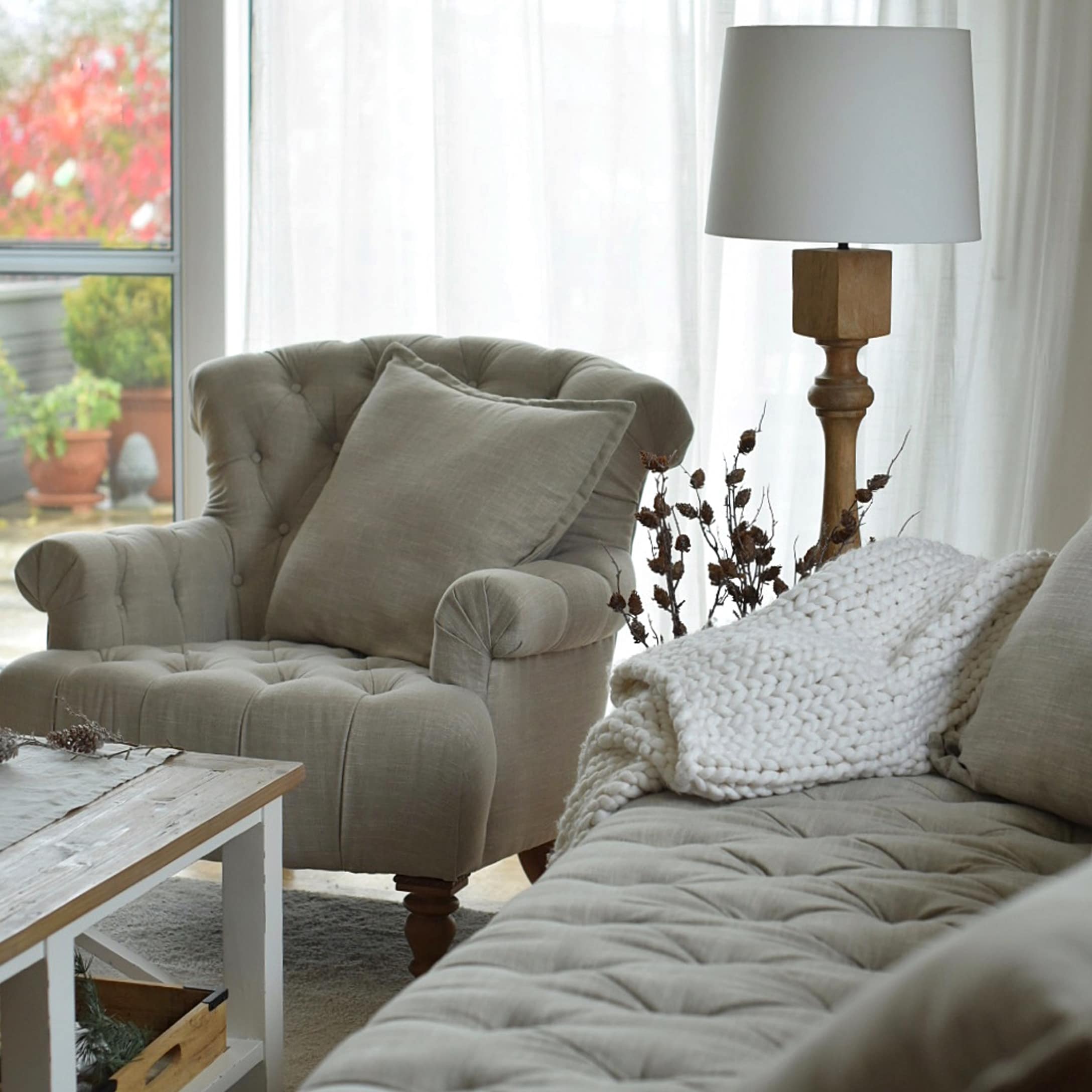 Beige gestoffeerde fauteuil en bank met kussens en witte gebreide deken in gezellige woonkamer