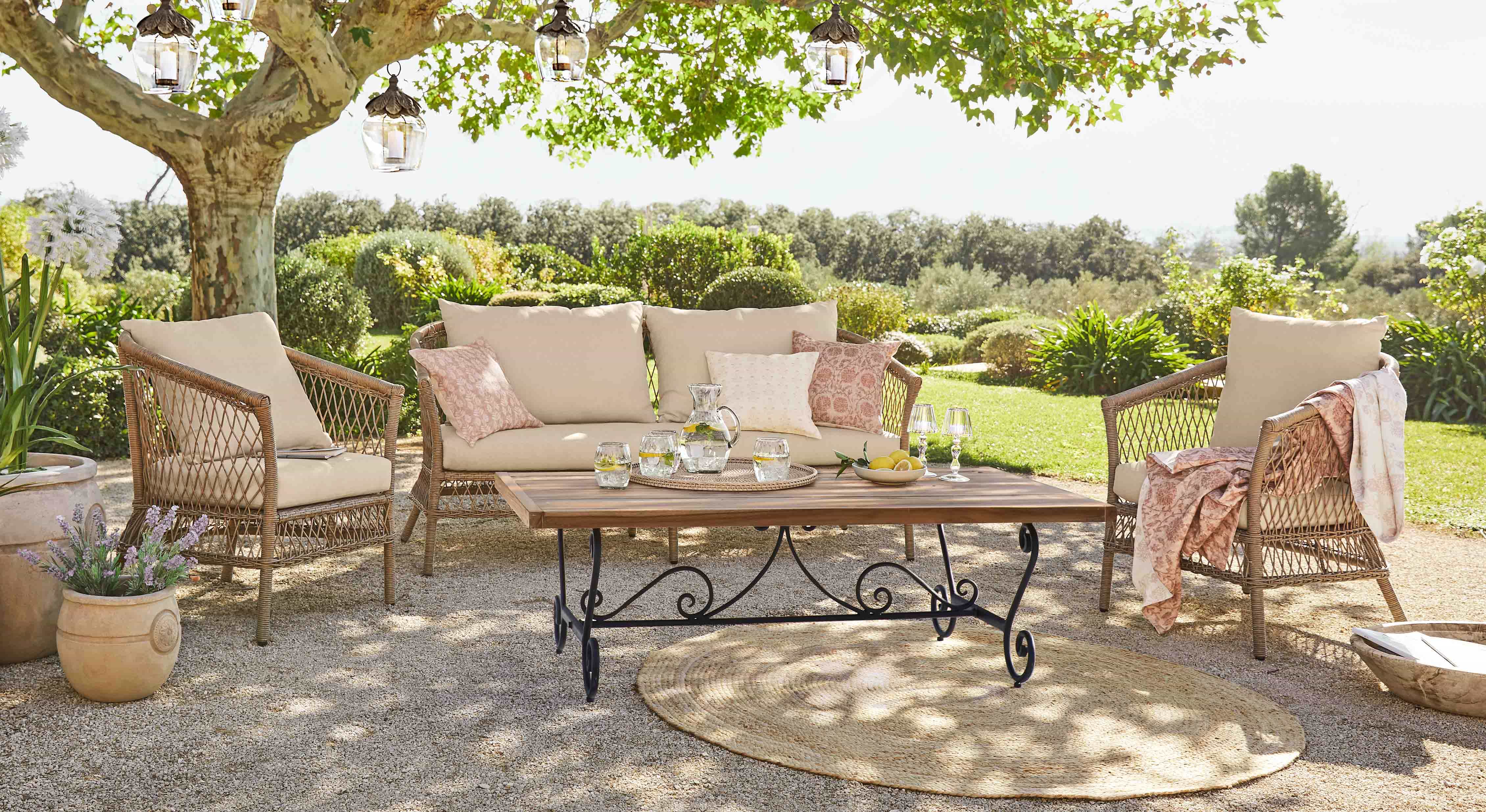 Tuinmeubelset van rattan met beige kussens en houten tafel op zonnig terras in tuin