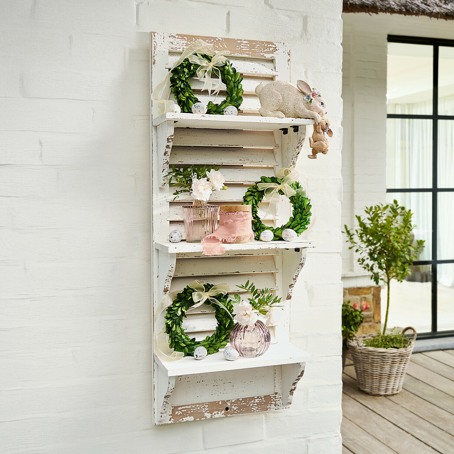 Witte houten wandplank met verweerde look, groene kransen en paasdecoraties