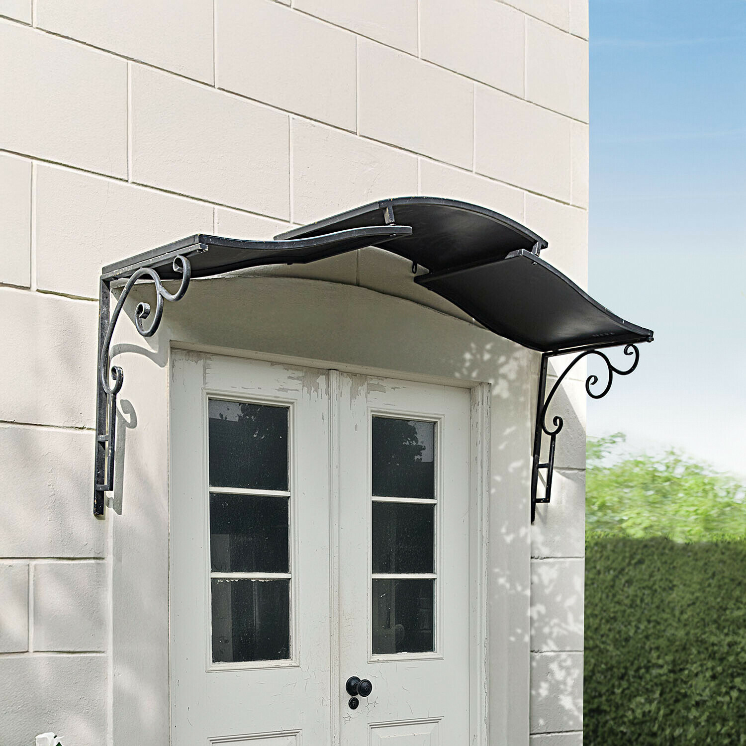 Zwart metalen luifel met sierlijke steunen boven witte dubbele deur met ramen