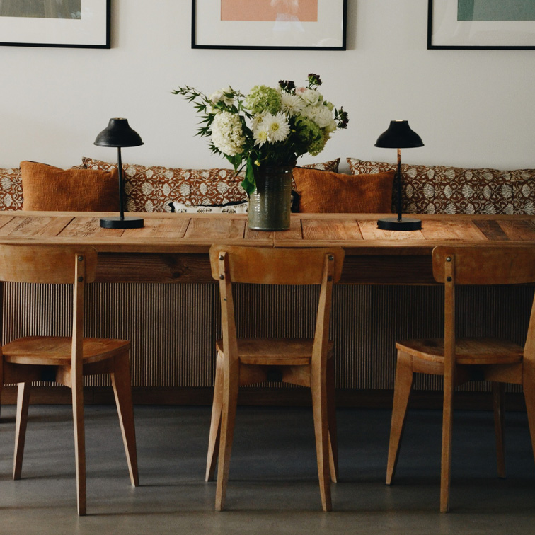 Houten tafel met drie stoelen, zwarte lampen en vaas met witte bloemen in gezellige woonkamer