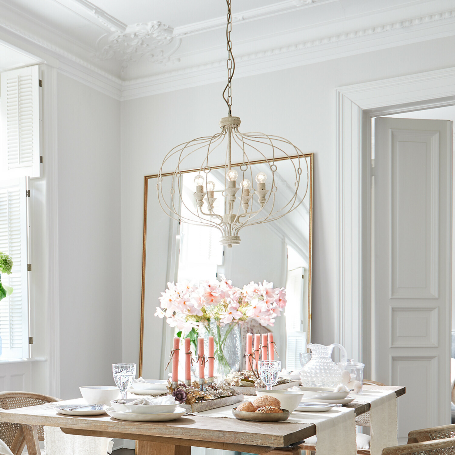 Lichte eetkamer met houten tafel, roze kaarsen en vintage metalen hanglamp aan het plafond
