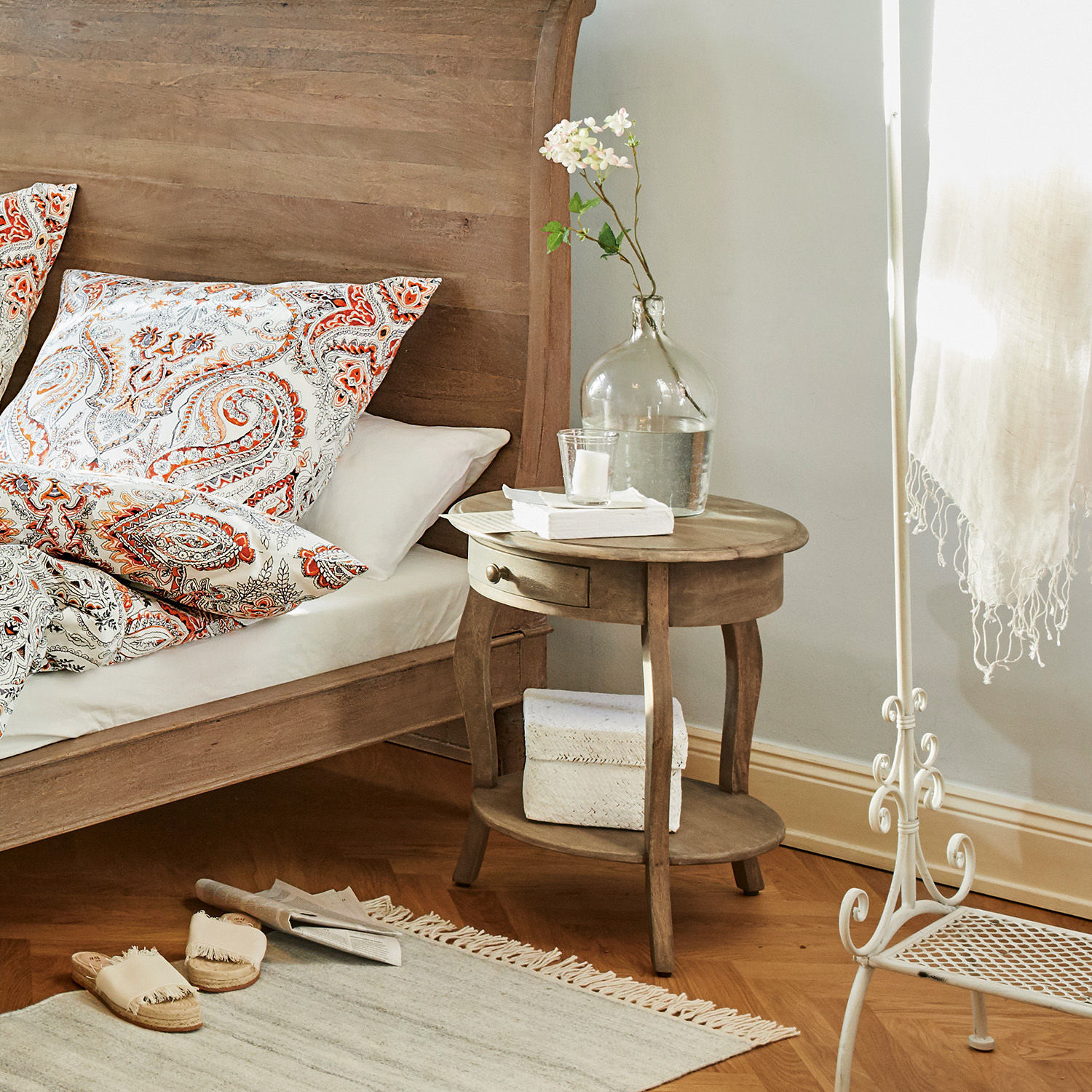 Ronde houten nachtkastje met lade en plank in lichte slaapkamer met decoratie en lamp