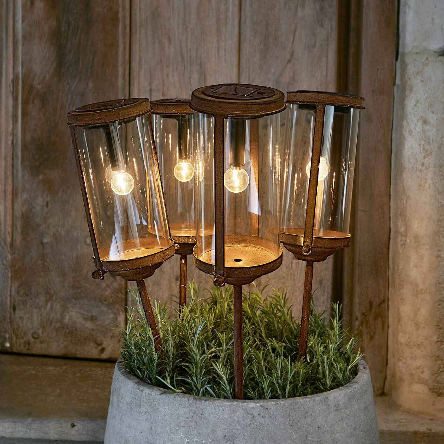 Set van vier roestige tuinlampen met glazen kappen en metalen standaards in een plantenpot