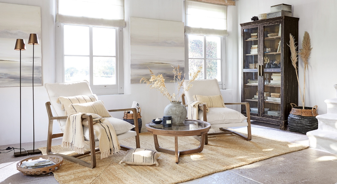Gezellige woonkamer met beige fauteuils, houten salontafel en donkere vitrinekast met boeken, natuurlijke decoratie