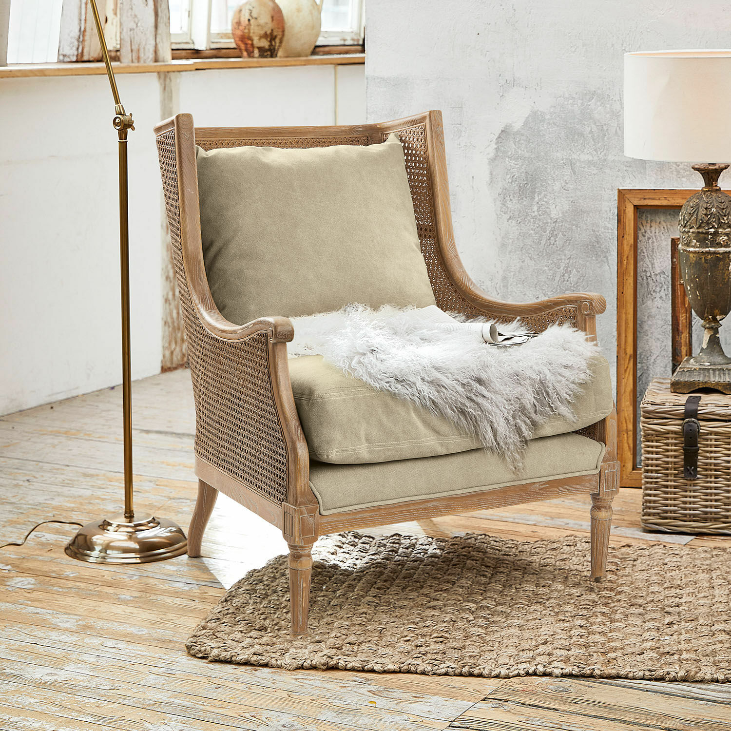 Fauteuil Greenbrier Stoel van hout en riet met beige kussen en witte bontdeken op natuurlijke vloerkleed