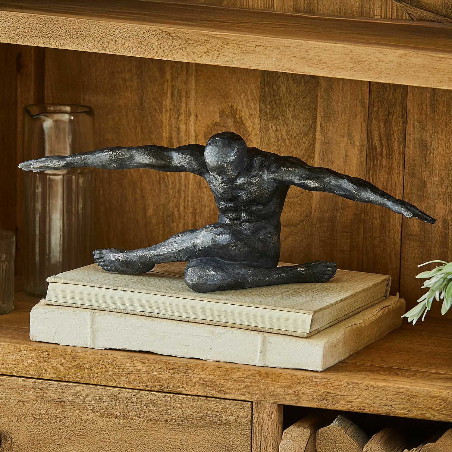 Zwarte sculptuur van een mannelijke figuur met uitgestrekte armen op boeken op een decoratieve houten plank