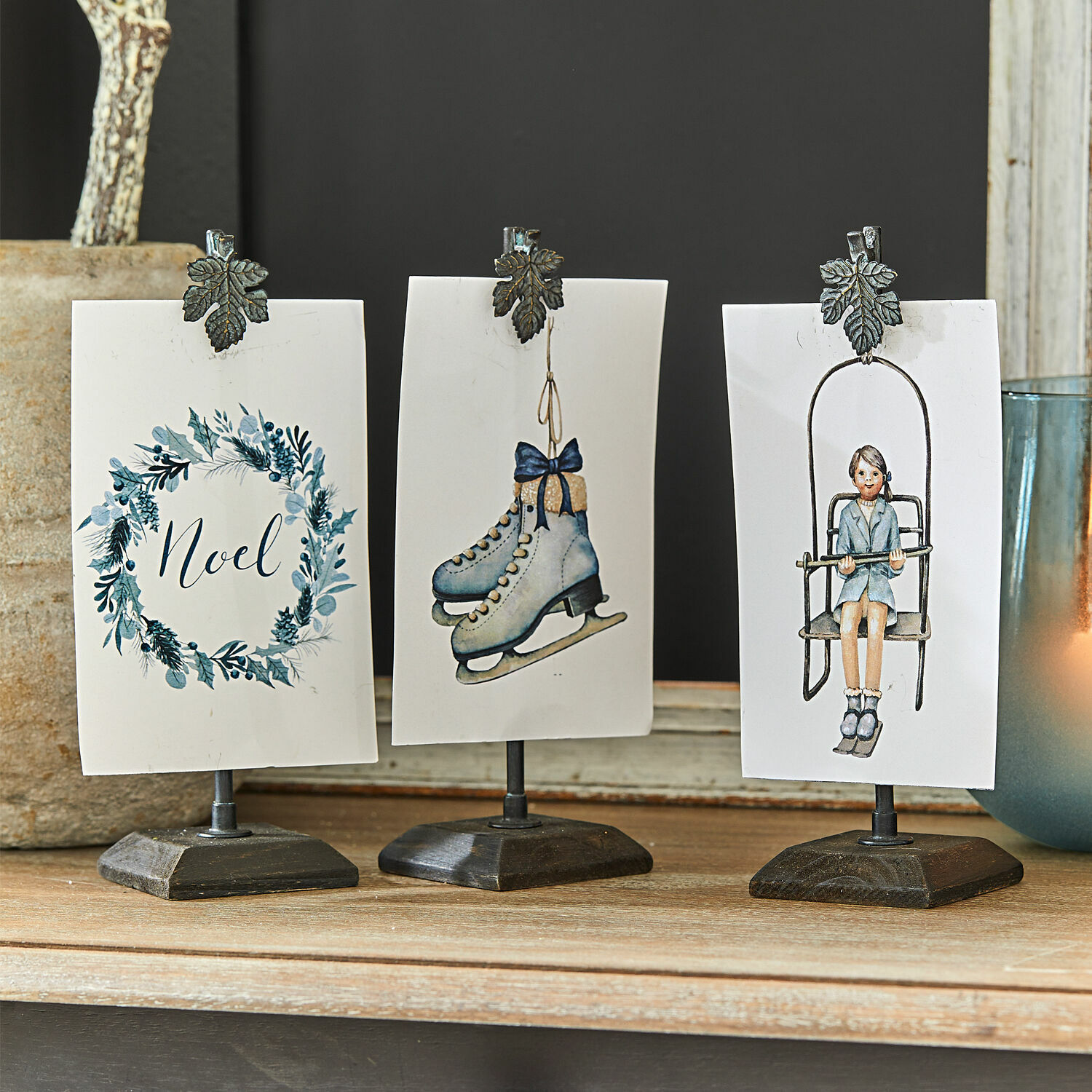 Drie metalen standaards met klemmen en winterse kaarten in blauw-witte tinten op houten ondergrond