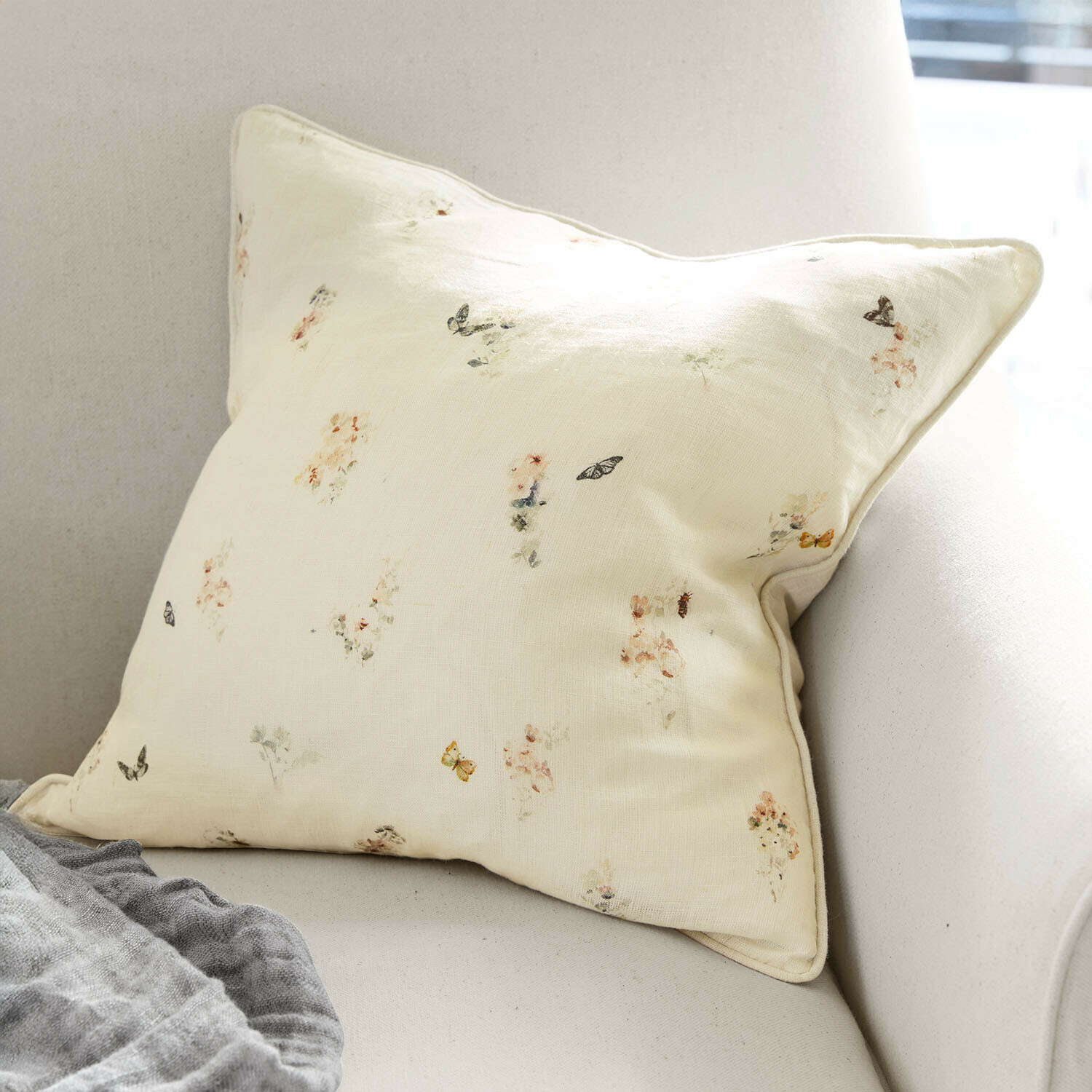 Kussenhoes Salénaïs Licht crèmekleurig kussen met subtiel bloemen- en vlindermotief op bank, interieurdecoratie