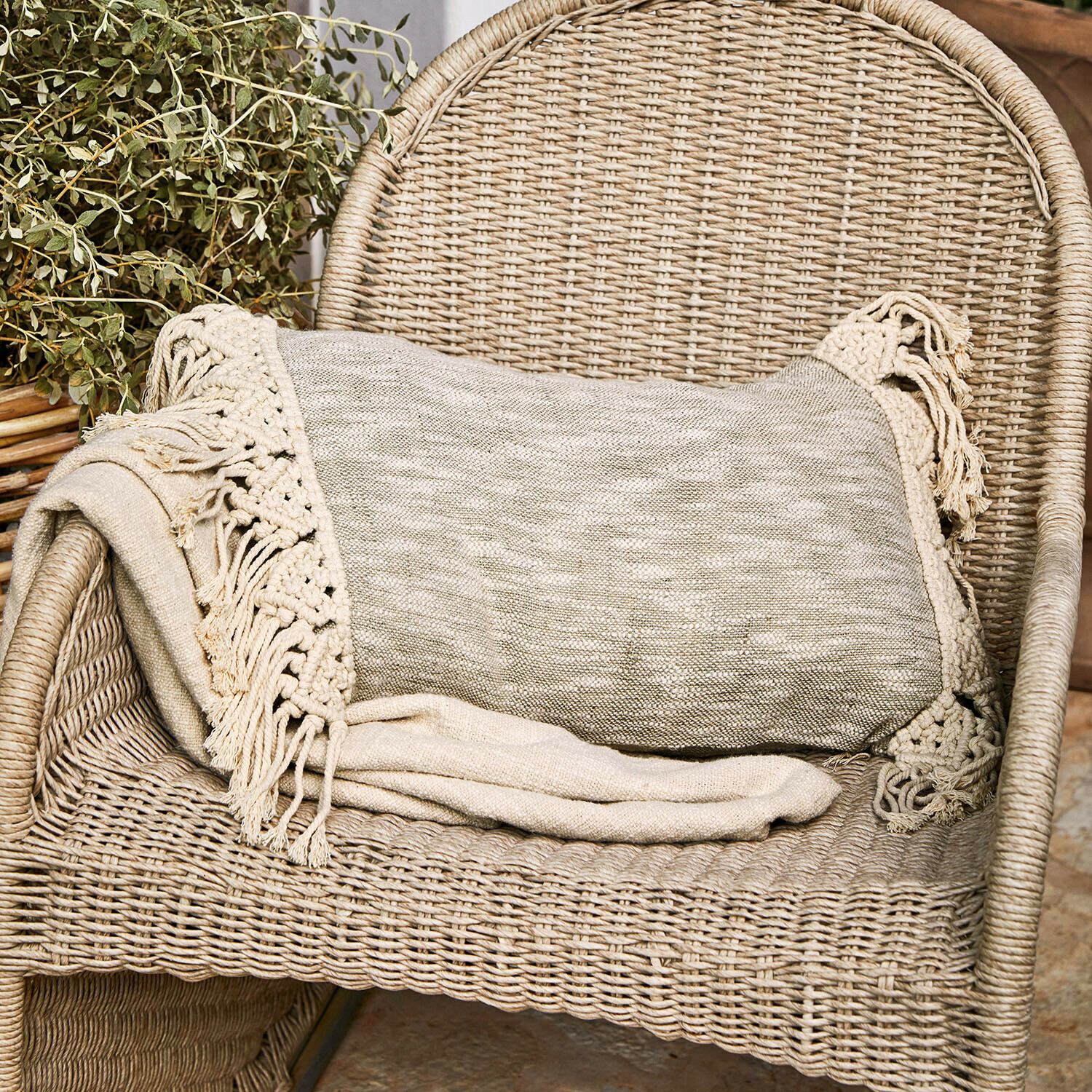 Kussenhoes Dunlora Beige deken met franjes op een rotan stoel, gezellige woondecoratie en textiel