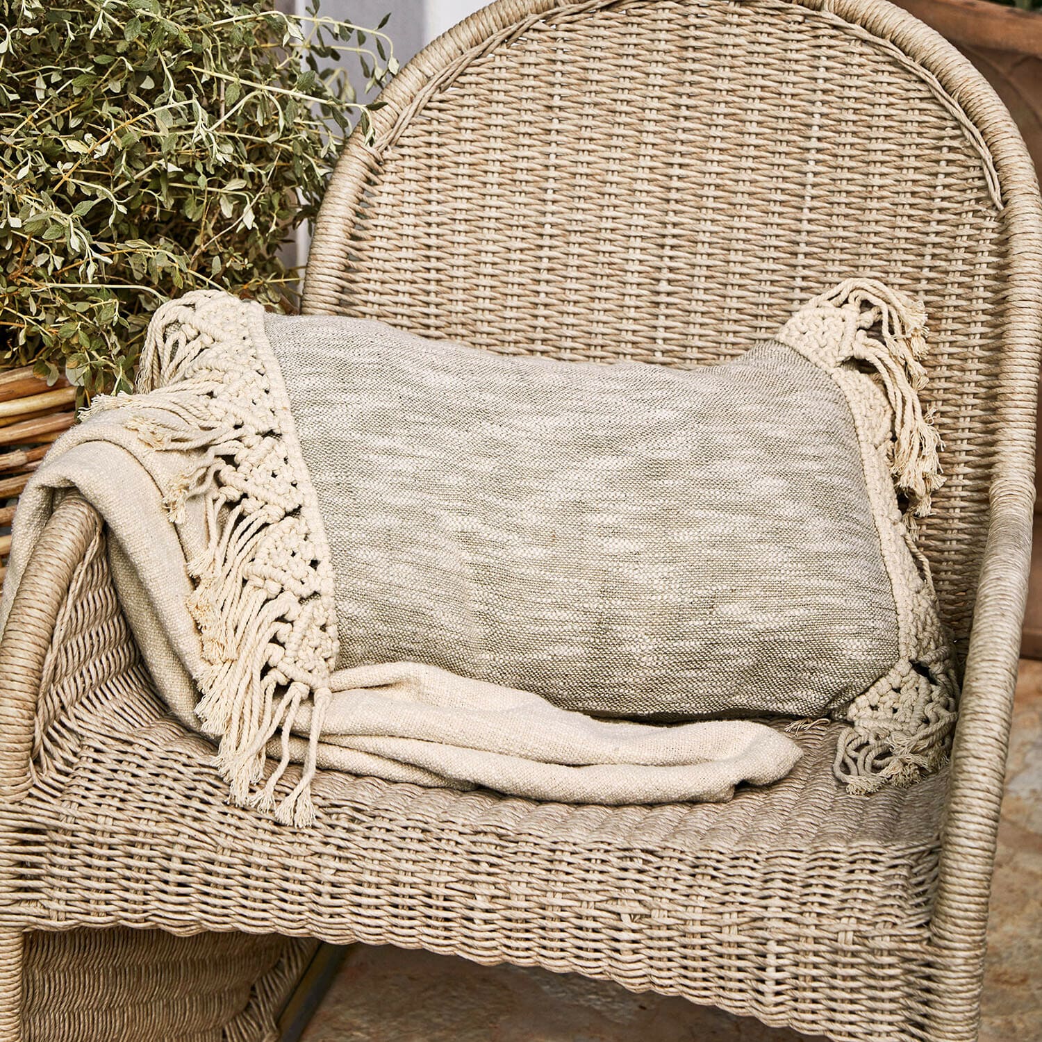 Kussenhoes Dunlora Beige deken met franjes op een rotan stoel, gezellige woondecoratie en textiel