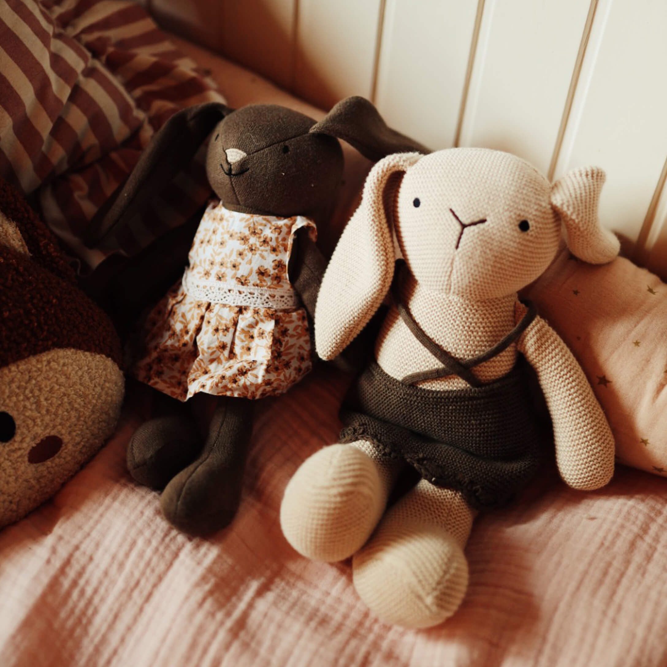 Twee zachte stoffen konijnen met jurkjes op roze beddengoed, knuffels voor kinderkamer