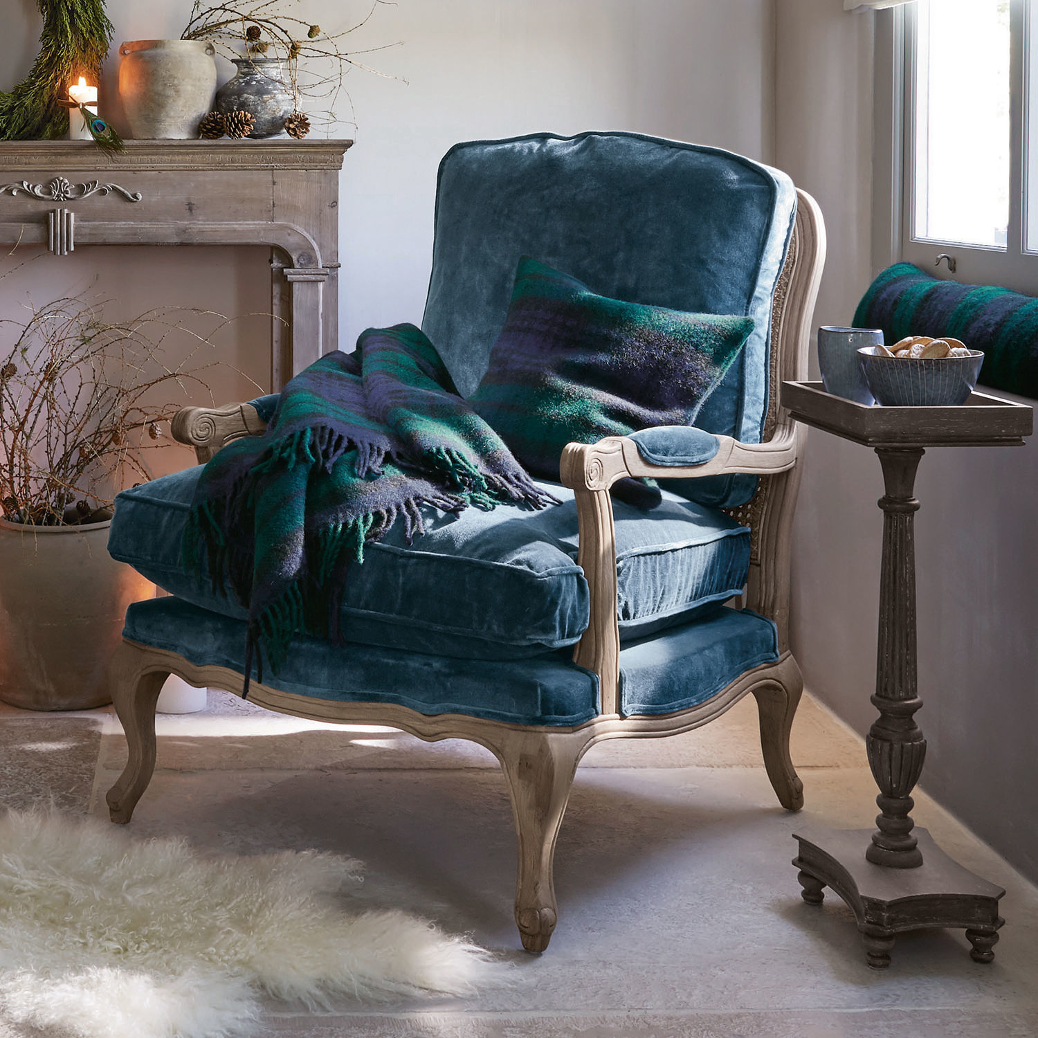 Fauteuil Corlay Blauwe fluwelen fauteuil met lichte houten frame, groene en blauwe deken en kussen in gezellige kamer