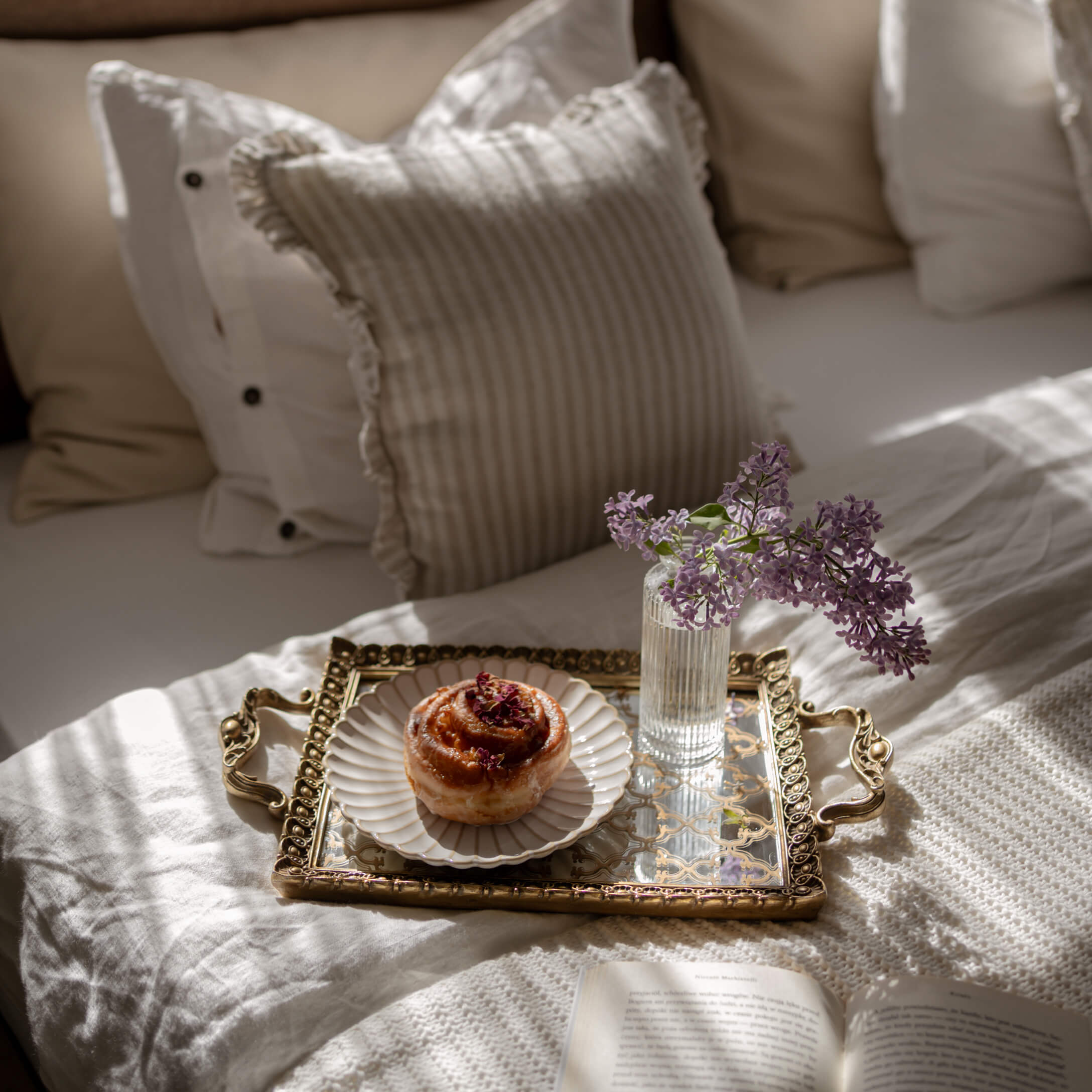 Gouden spiegel dienblad met wit porseleinen bord, gebak en vaas met paarse bloemen op bed