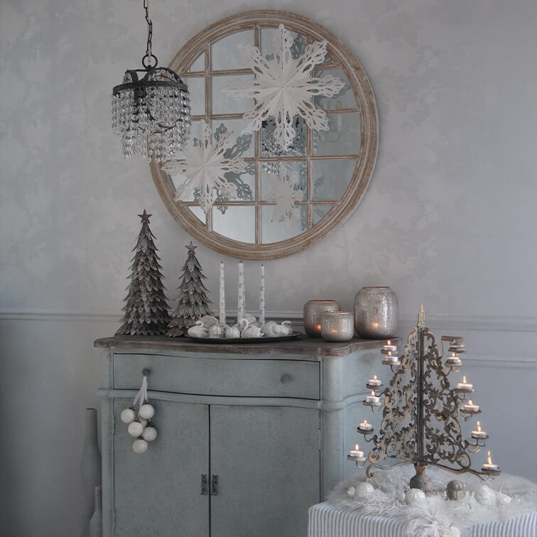 Grijze kast met kerstdecoraties, metalen kerstbomen en vintage kandelaar met brandende kaarsen