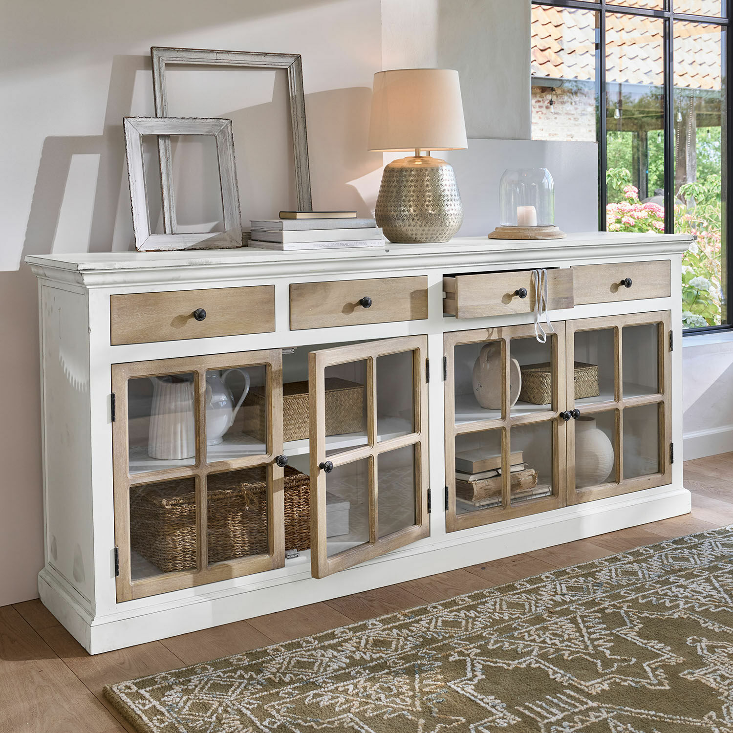 Witte houten dressoir met lades en glazen deuren, decoraties en lamp erop geplaatst