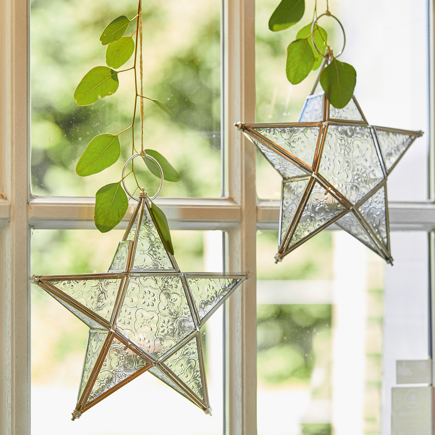 Windlicht set van 2 Kian Glazen sterren met metalen frame hangend aan raam met groene bladeren