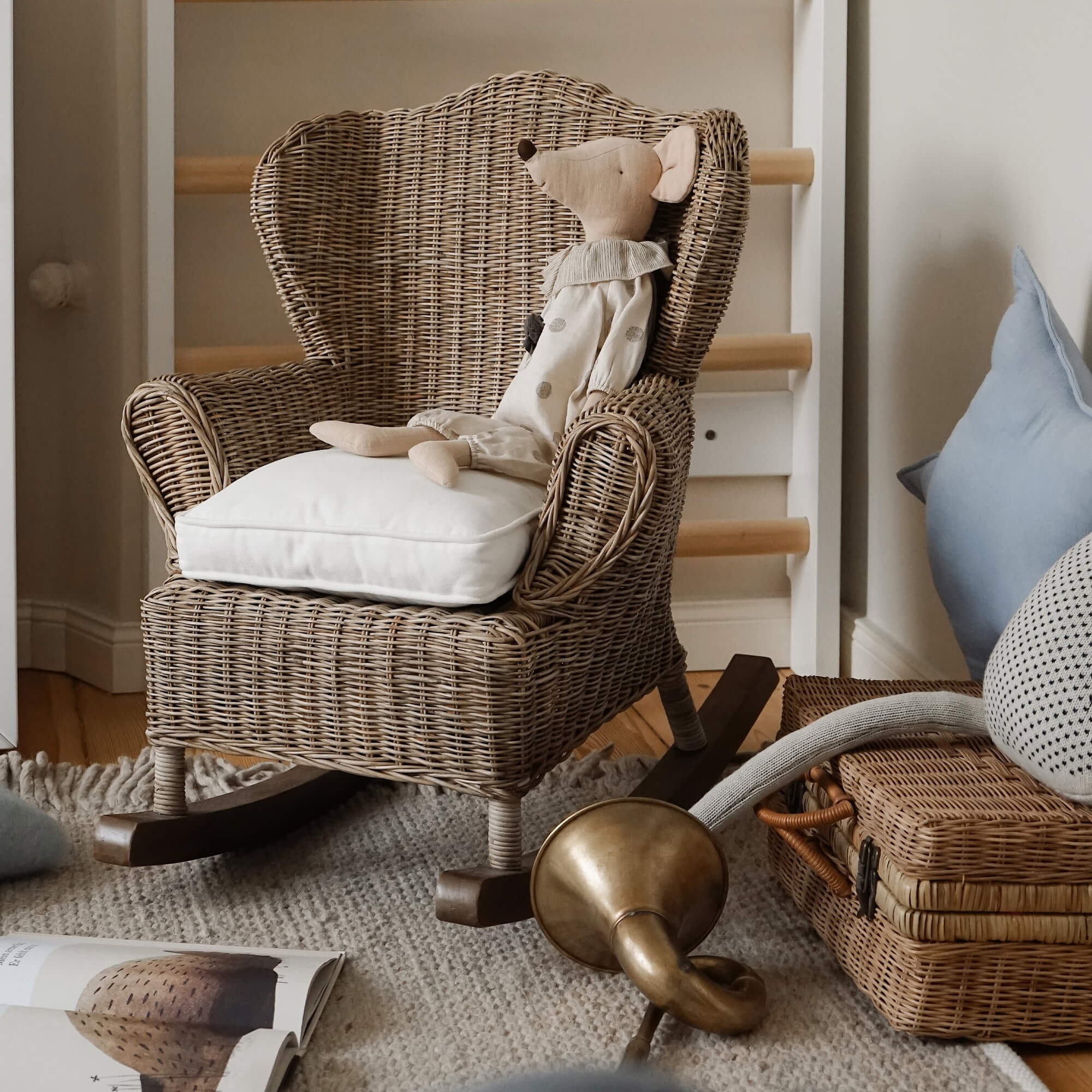 Rotan schommelstoel met wit kussen en pluchen muis in natuurlijke kinderkamer