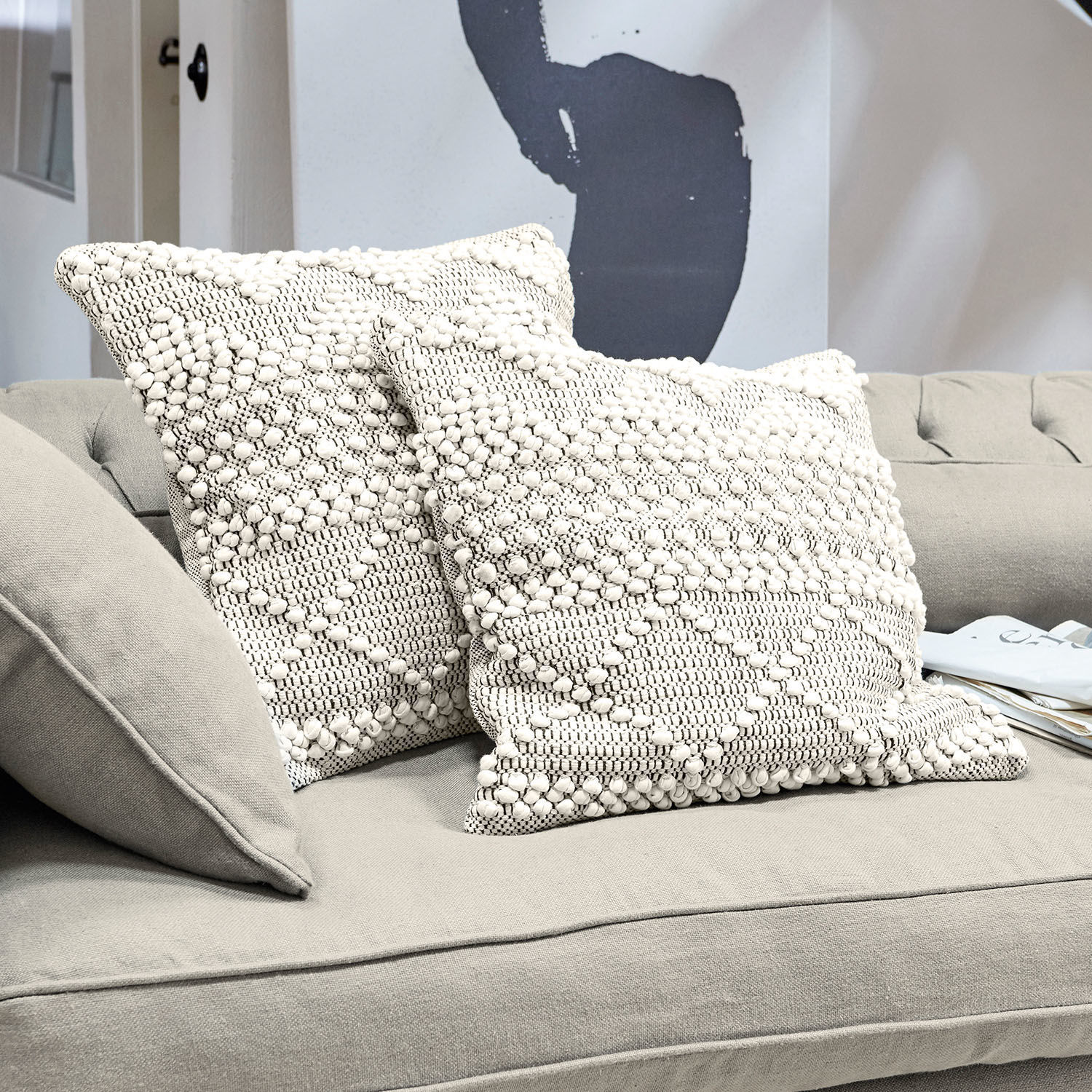 Twee crèmekleurige katoenen sierkussens met textuur en geometrisch patroon op een grijze bank