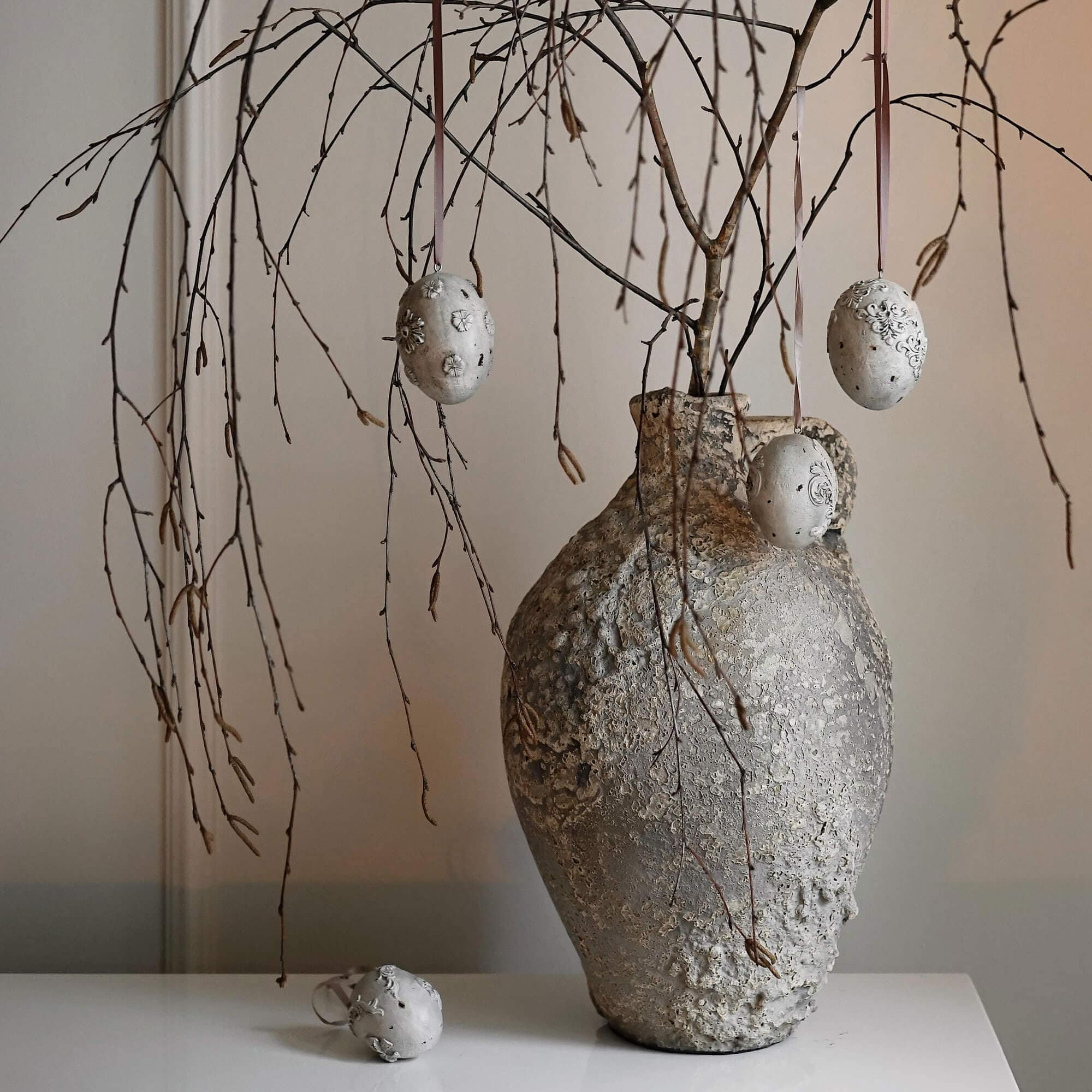 Rustieke grijze textuurvaas met takken en decoratieve hangende ei-ornamenten
