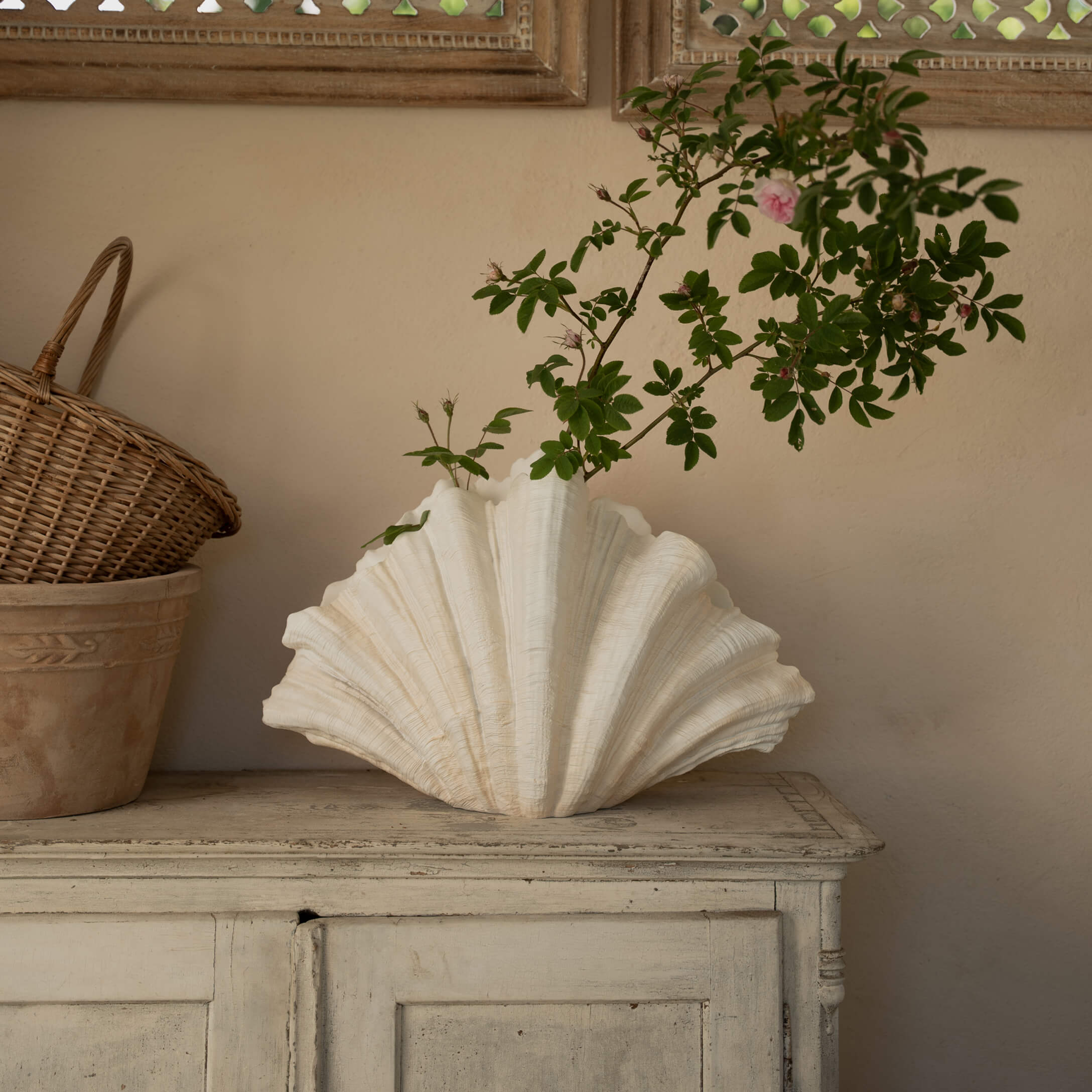 Witte keramische schelpvaas met groene takken op een houten kastje