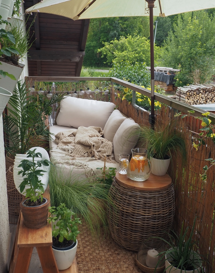 Gezellig balkon met beige bank, kussens, rotan tafel, planten en parasol voor buitenontspanning