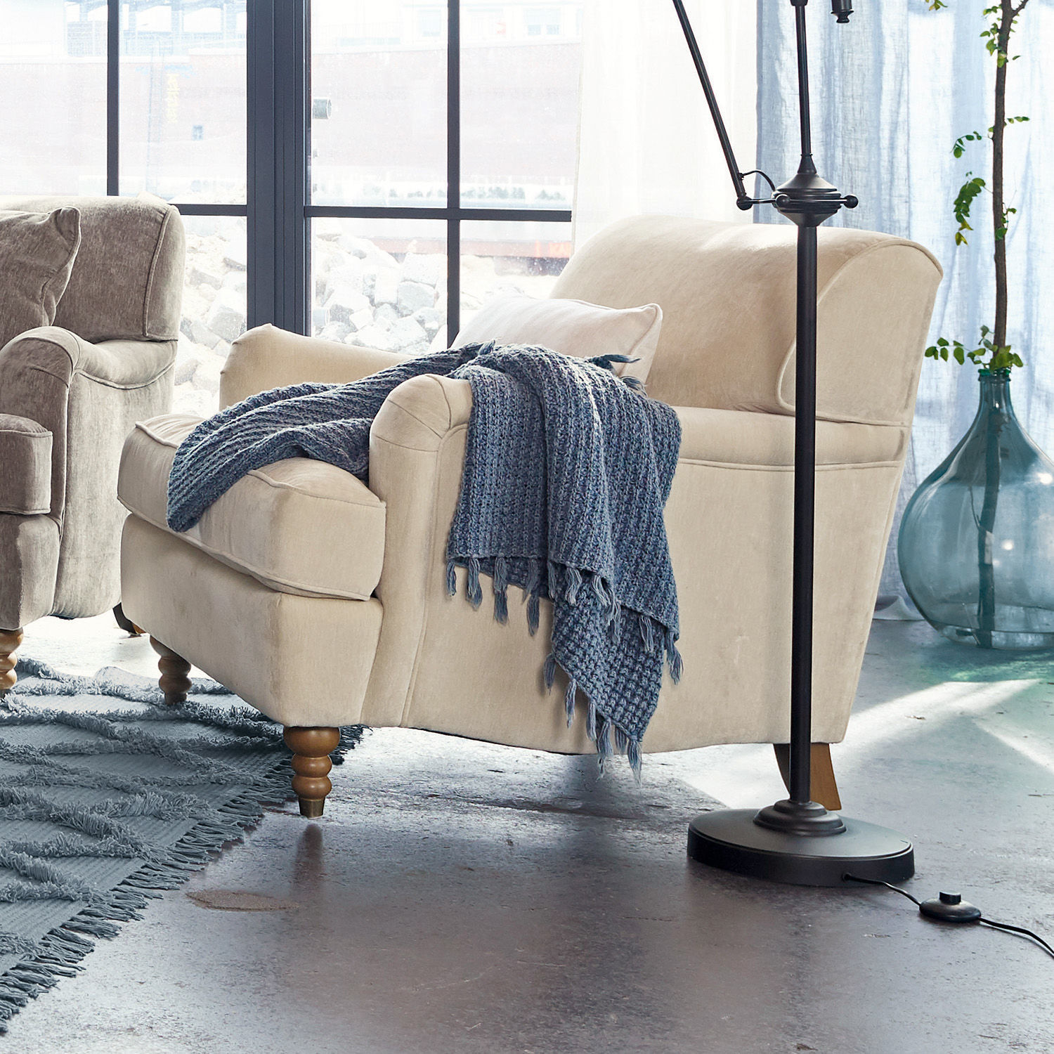 Beige gestoffeerde fauteuil met houten poten en blauwe gebreide deken in moderne woonkamer