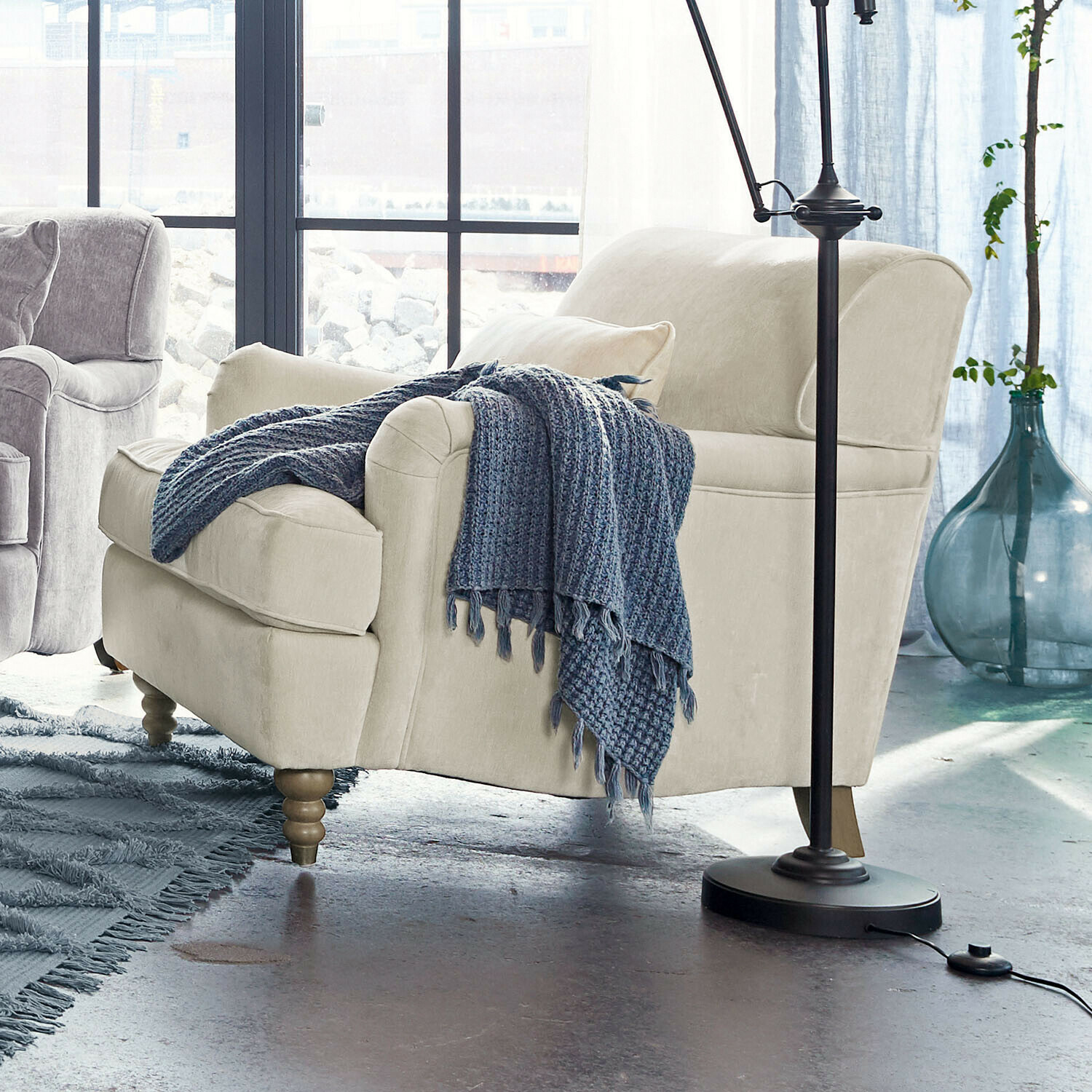 Beige gestoffeerde fauteuil met houten poten en blauwe gebreide deken in moderne woonkamer