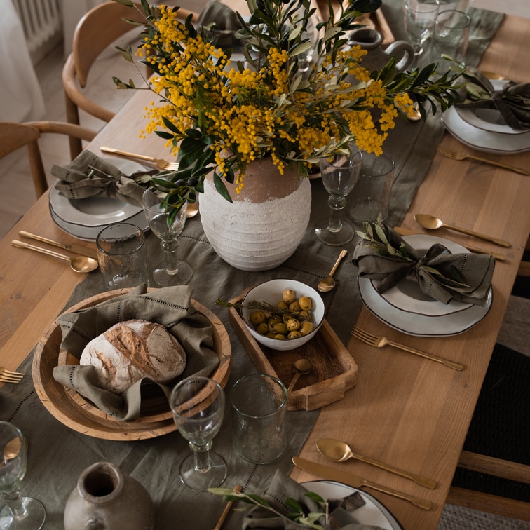 Rustieke houten tafel met wit servies, houten kommen en gele bloemen in een aardewerken vaas