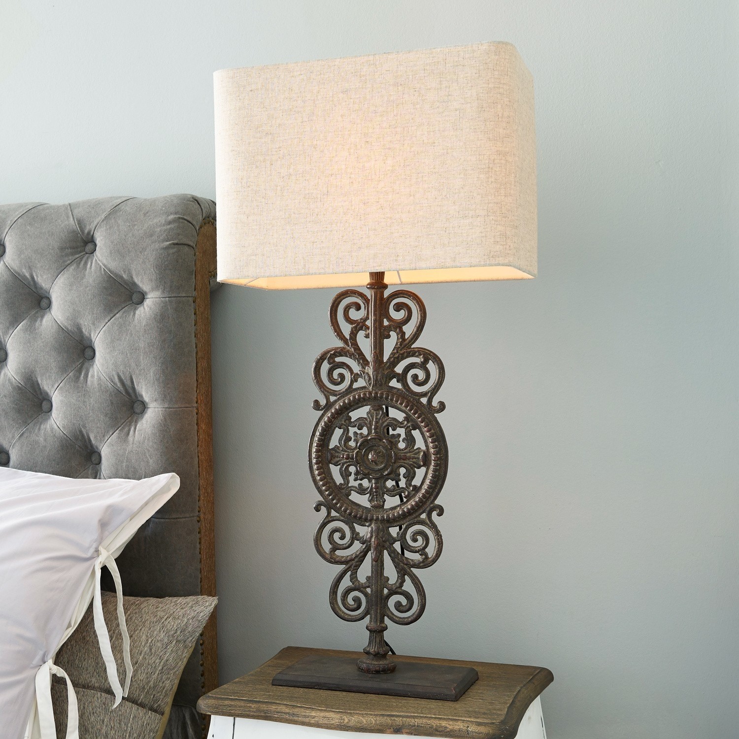 Tafellamp met decoratieve metalen voet en beige lampenkap op nachtkastje