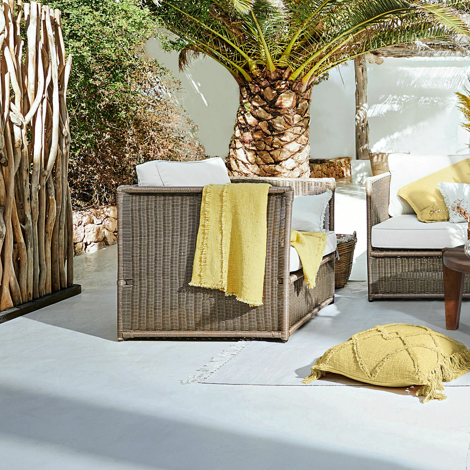 Fauteuil Lesmont Bruin rieten tuinmeubelset met witte kussens en gele accenten op zonnig terras