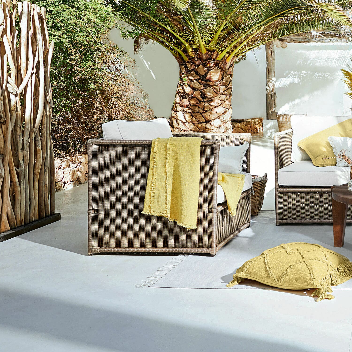 Fauteuil Lesmont Bruin rieten tuinmeubelset met witte kussens en gele accenten op zonnig terras