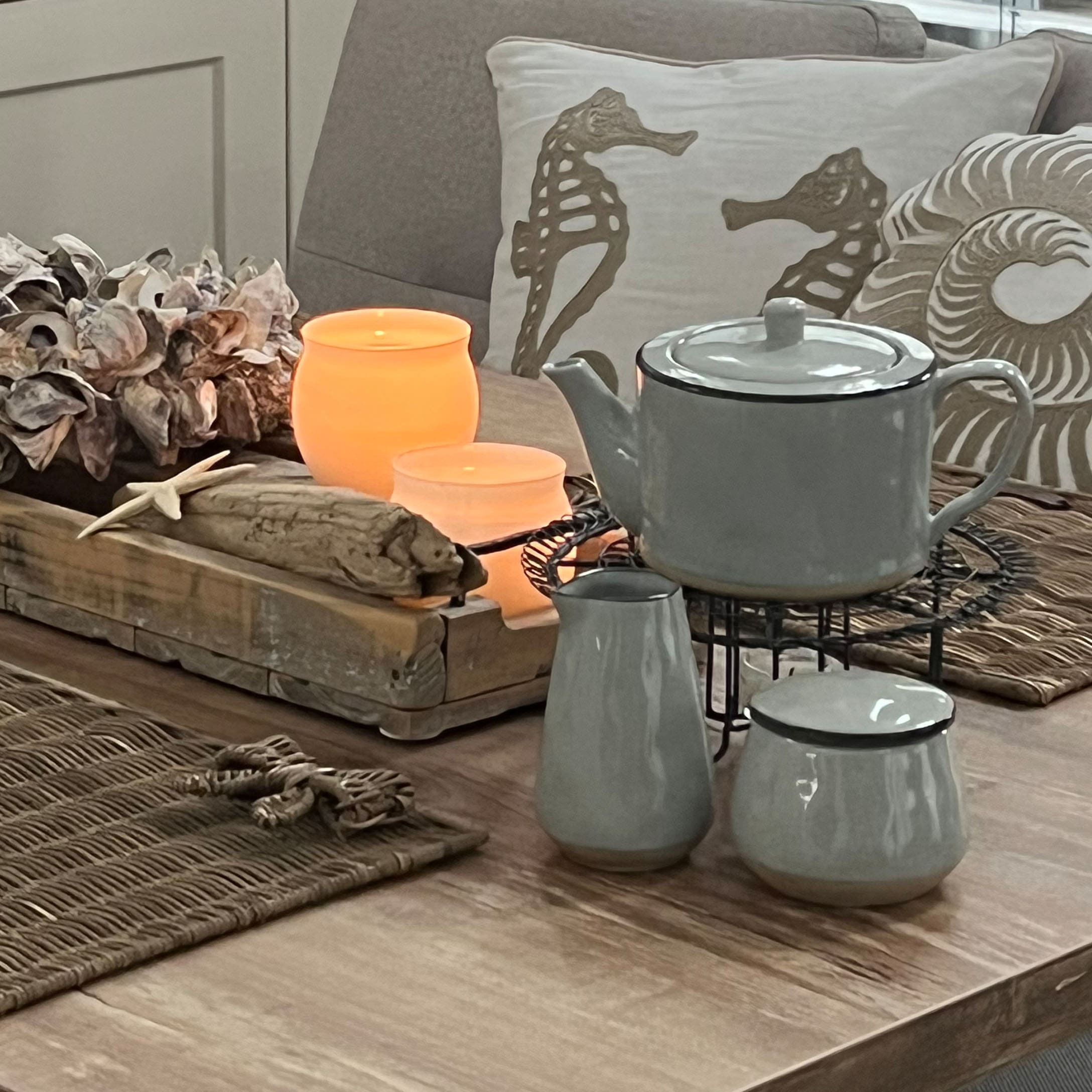Grijs keramisch theeservies op houten tafel met maritieme decoraties en brandende kaarsen