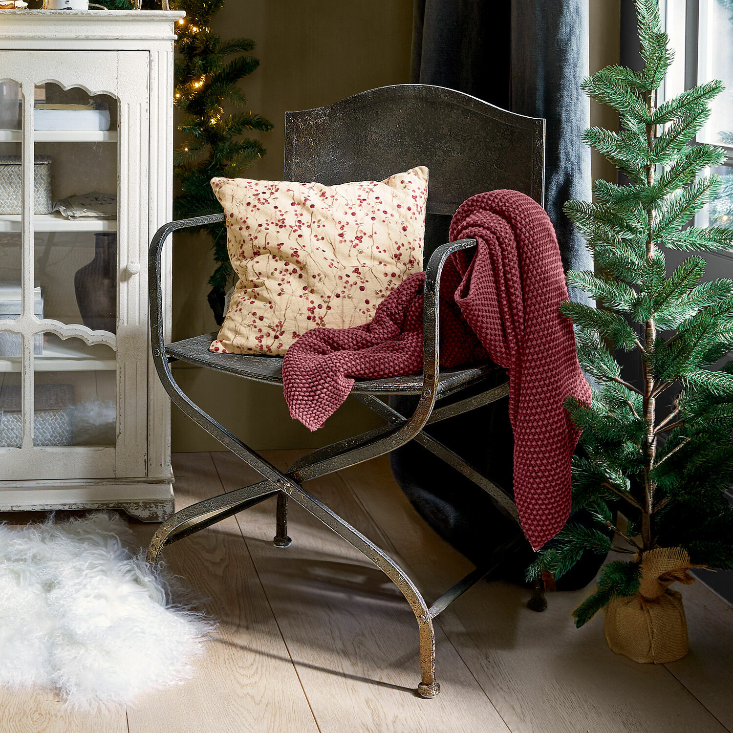 Metalen stoel met kussen met rode bessen en bordeauxrode deken in gezellige kamer met kerstboom