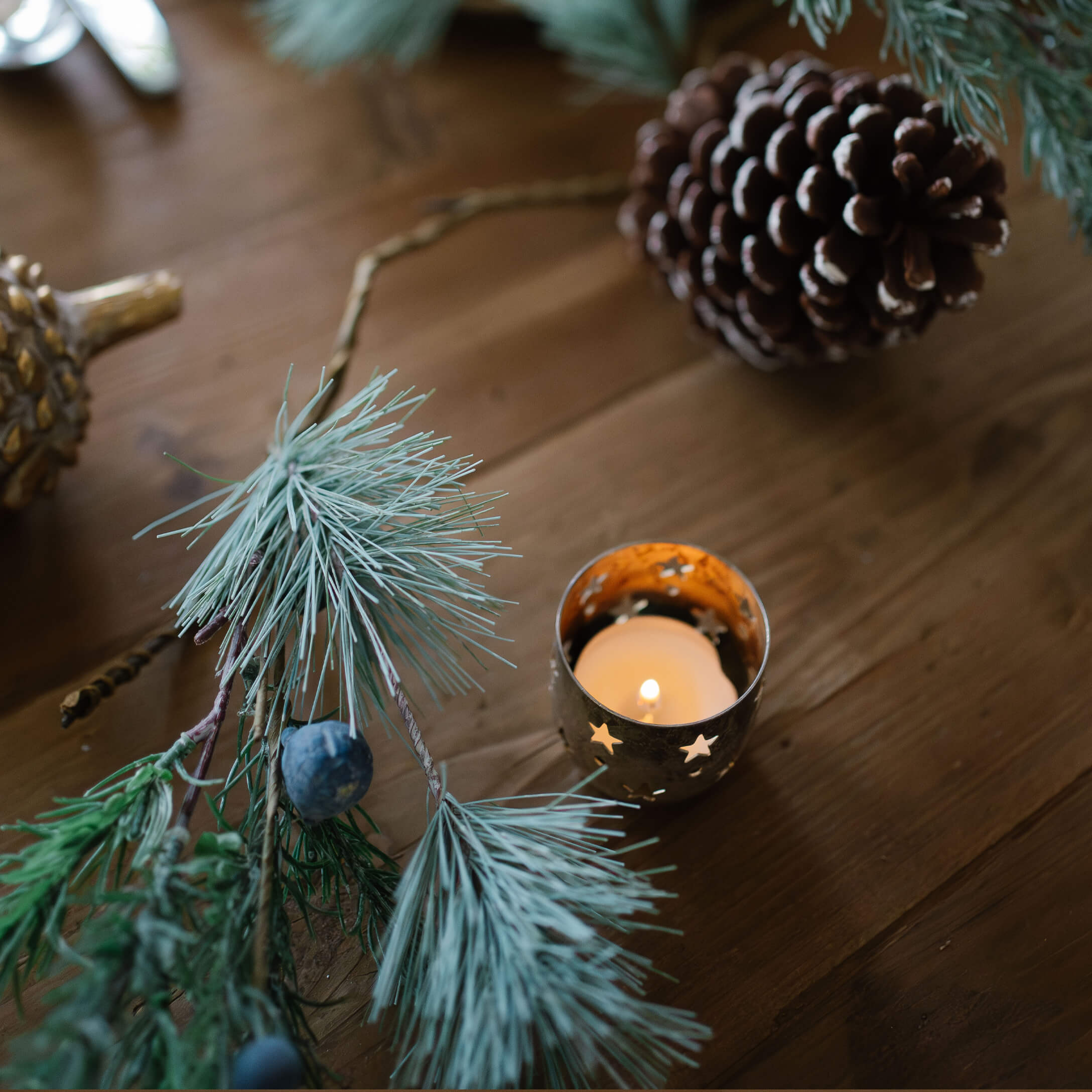 Metalen theelichthouder met uitgesneden sterren en brandende kaars op houten tafel met dennenappels en takken