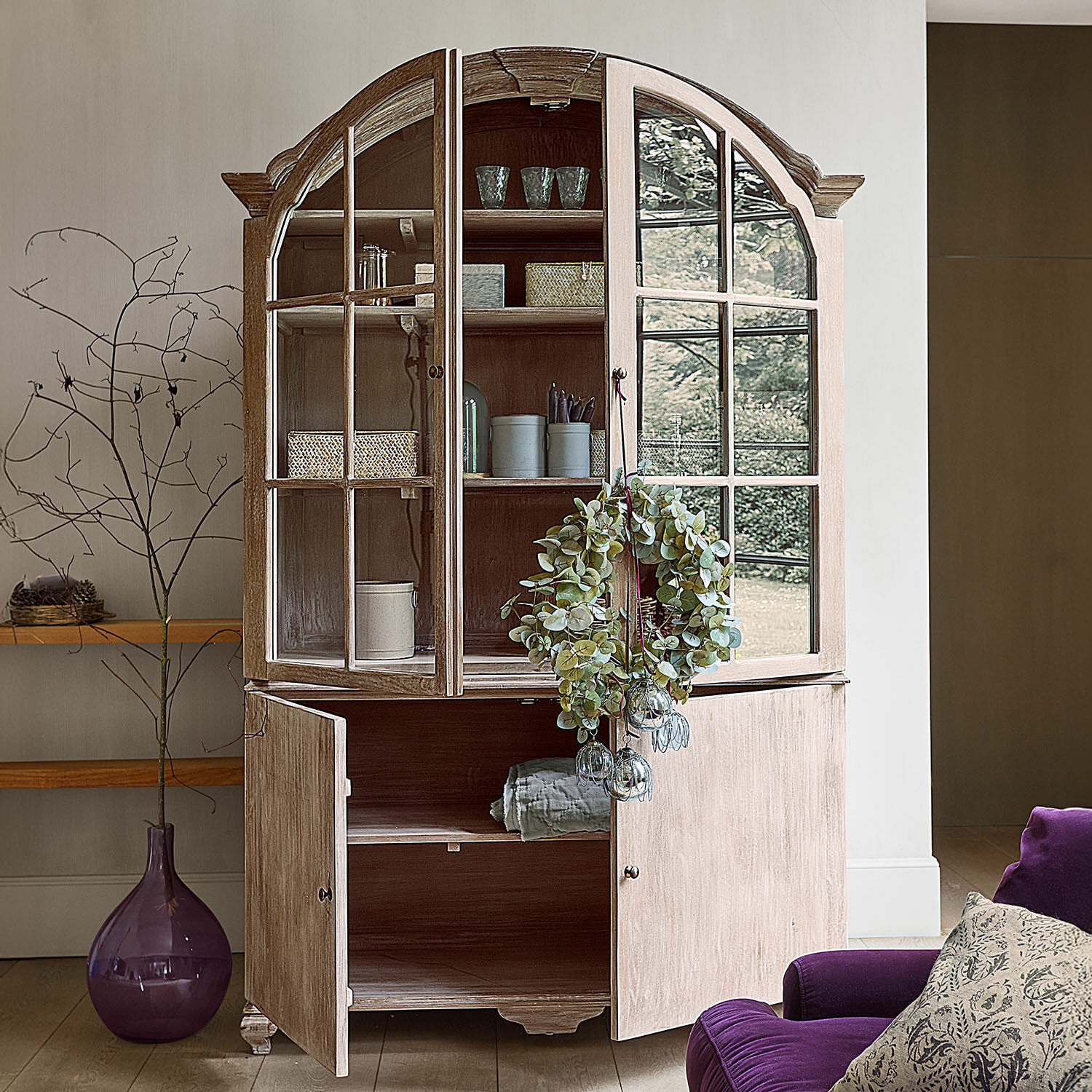 Lichte houten vitrinekast met glazen deuren en decoratieve krans, stijlvolle woonkamermeubel
