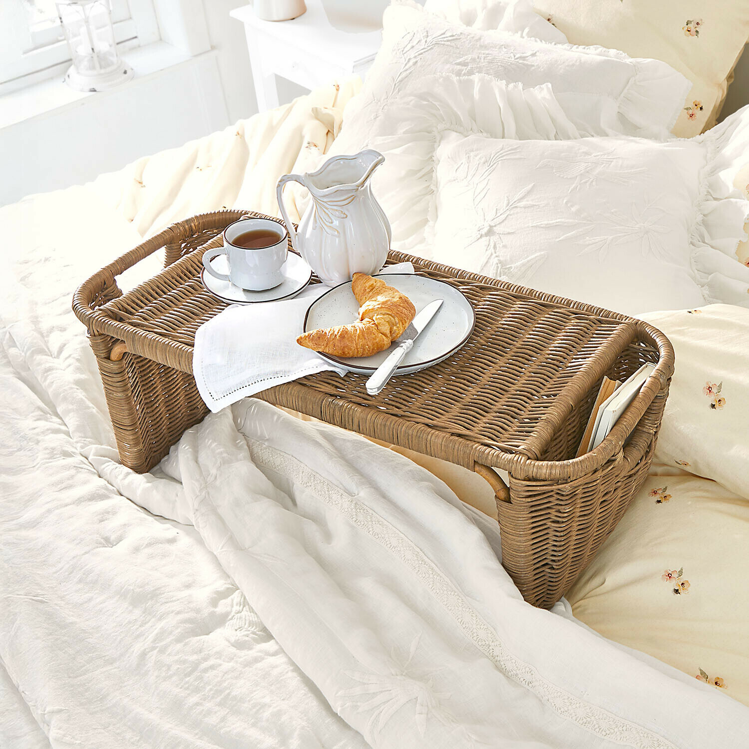 Bruine rieten ontbijttafel met wit servies en croissant op licht bed in slaapkamer