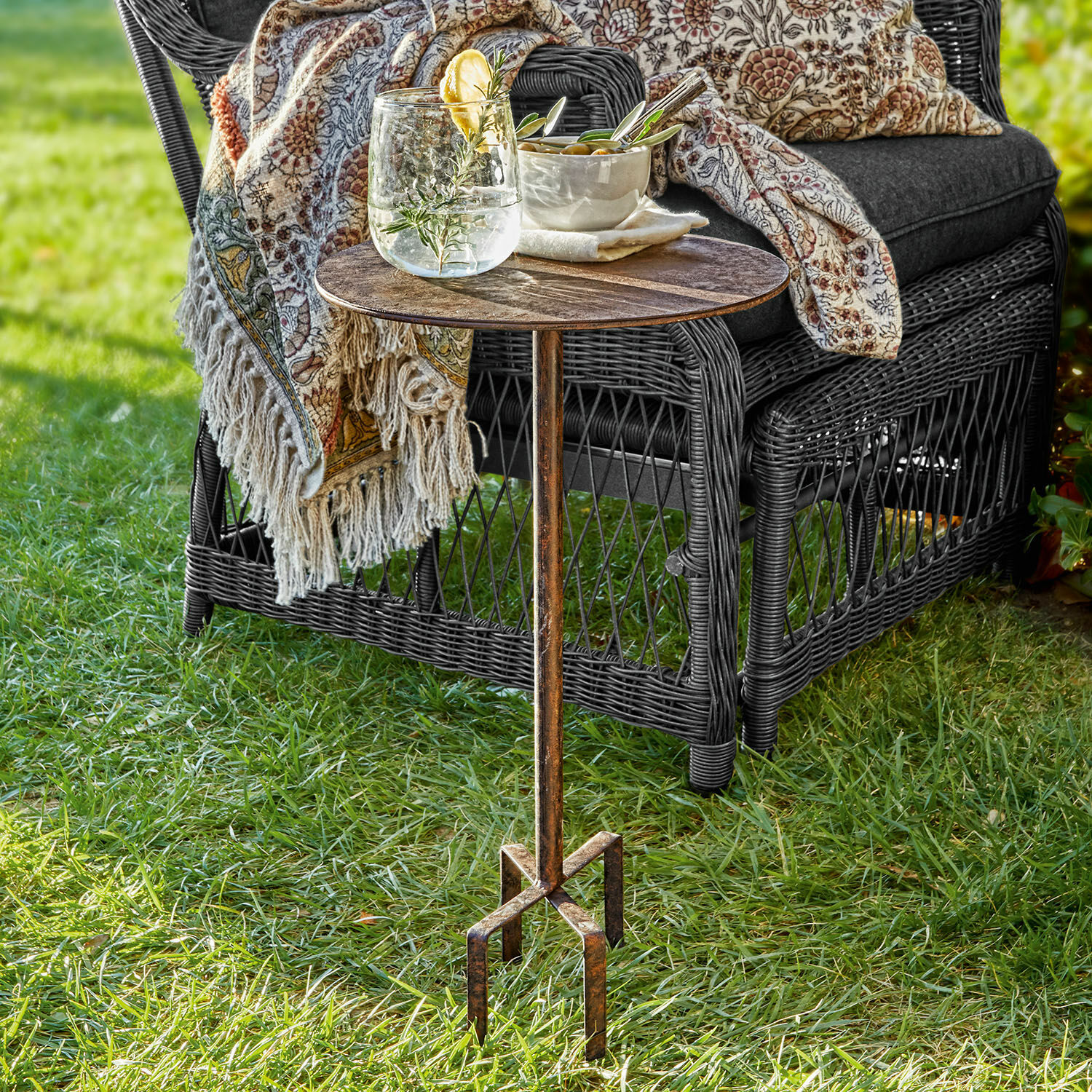 Tafeltje Fermont Metalen bijzettafel met vintage patina op gras naast een rotan stoel met kussen en deken