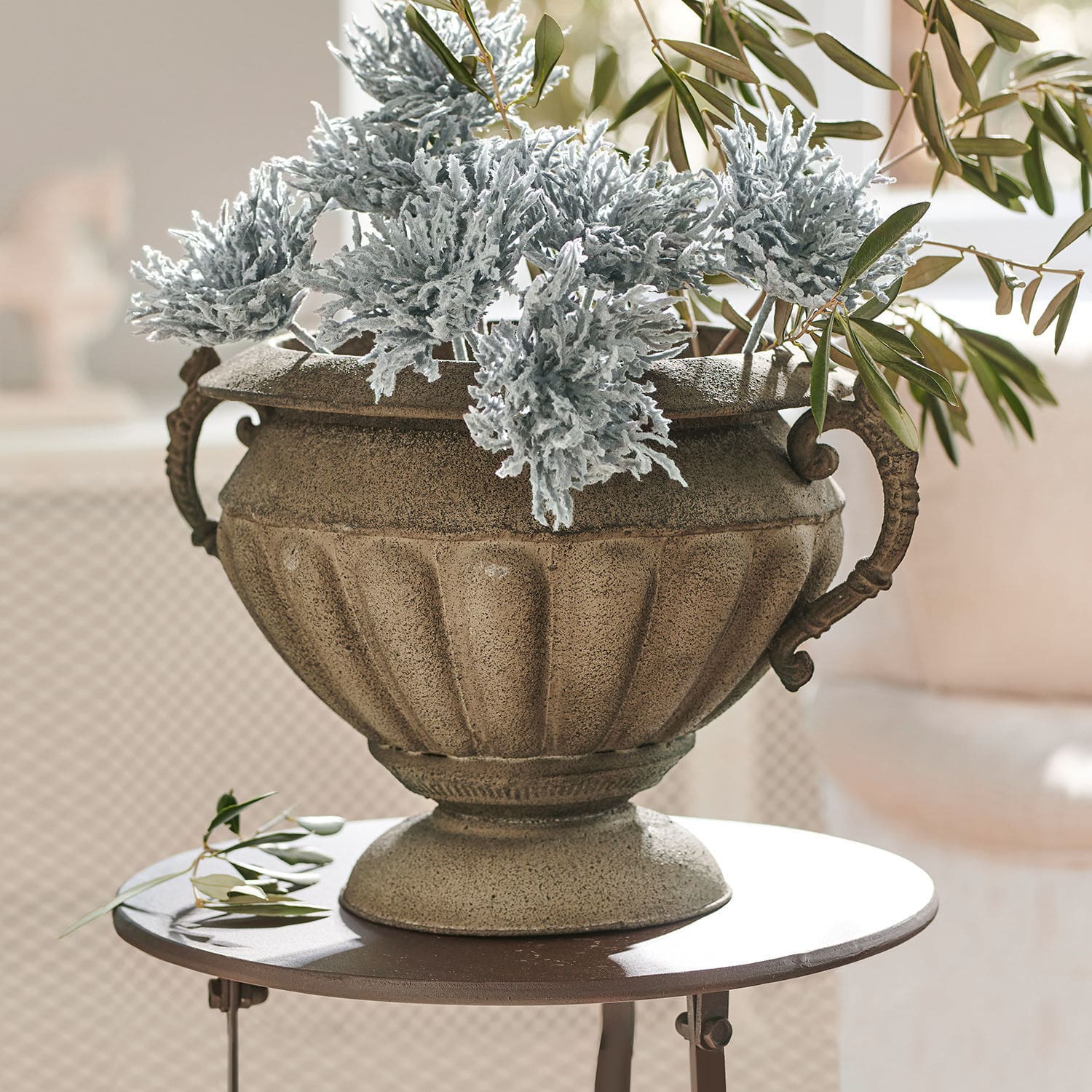 Amfoor Acheville Decoratieve stenen pot in beige met groene en grijze bladeren op een ronde tafel