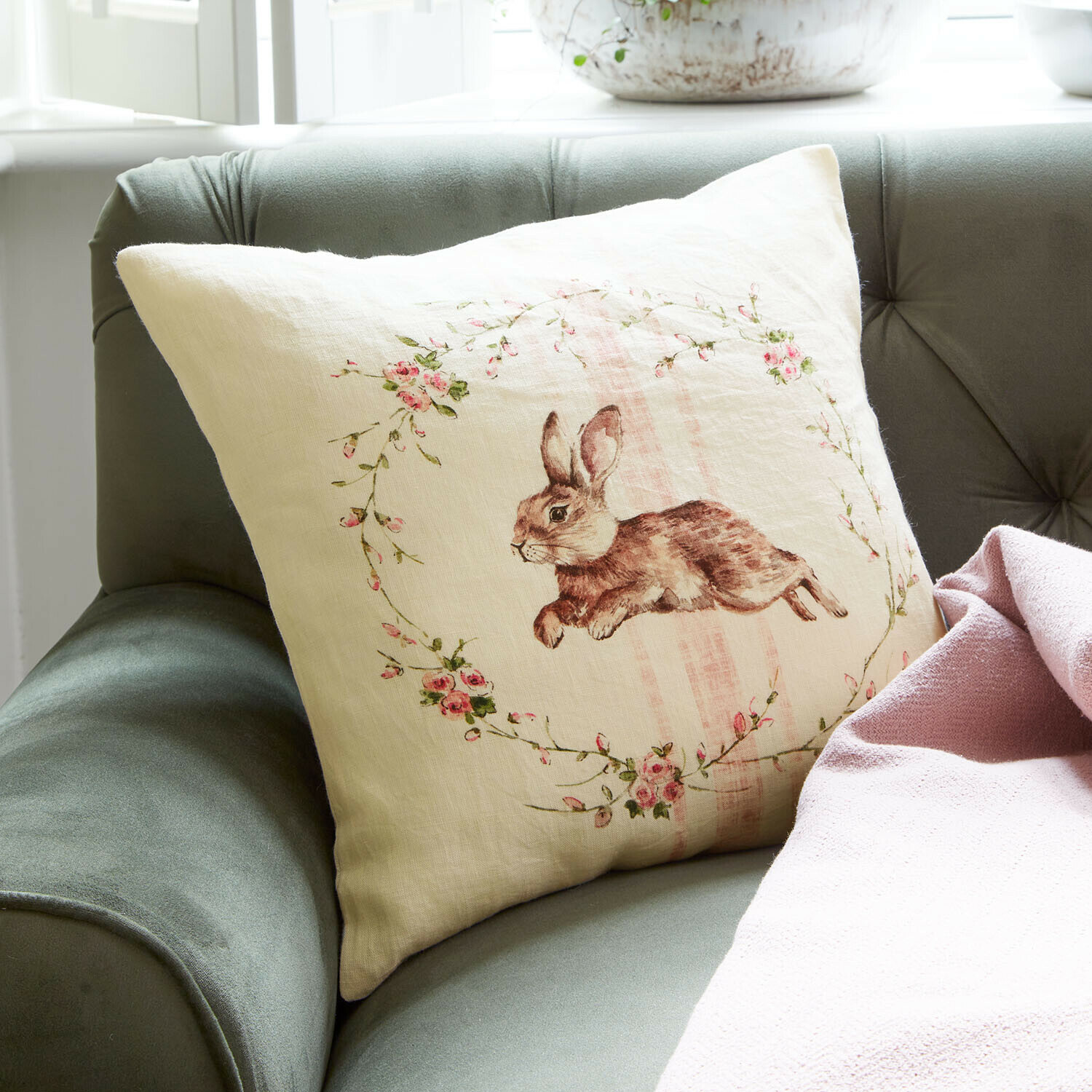 Kussenhoes Ravencrest Beige linnen kussen met konijnenprint en roze bloemen op groene bank met roze deken