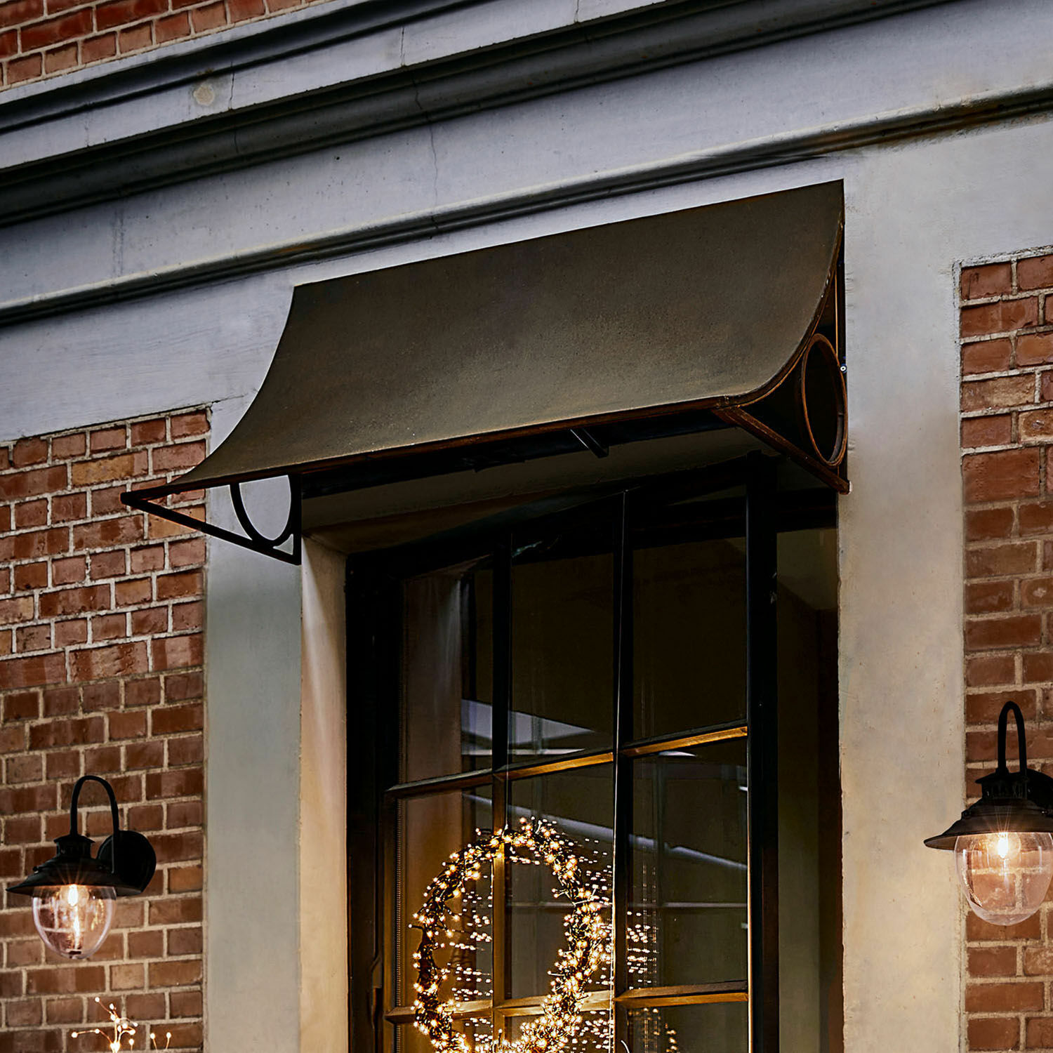 Olijfgroene metalen luifel boven raam met zwart frame en zwarte wandlampen