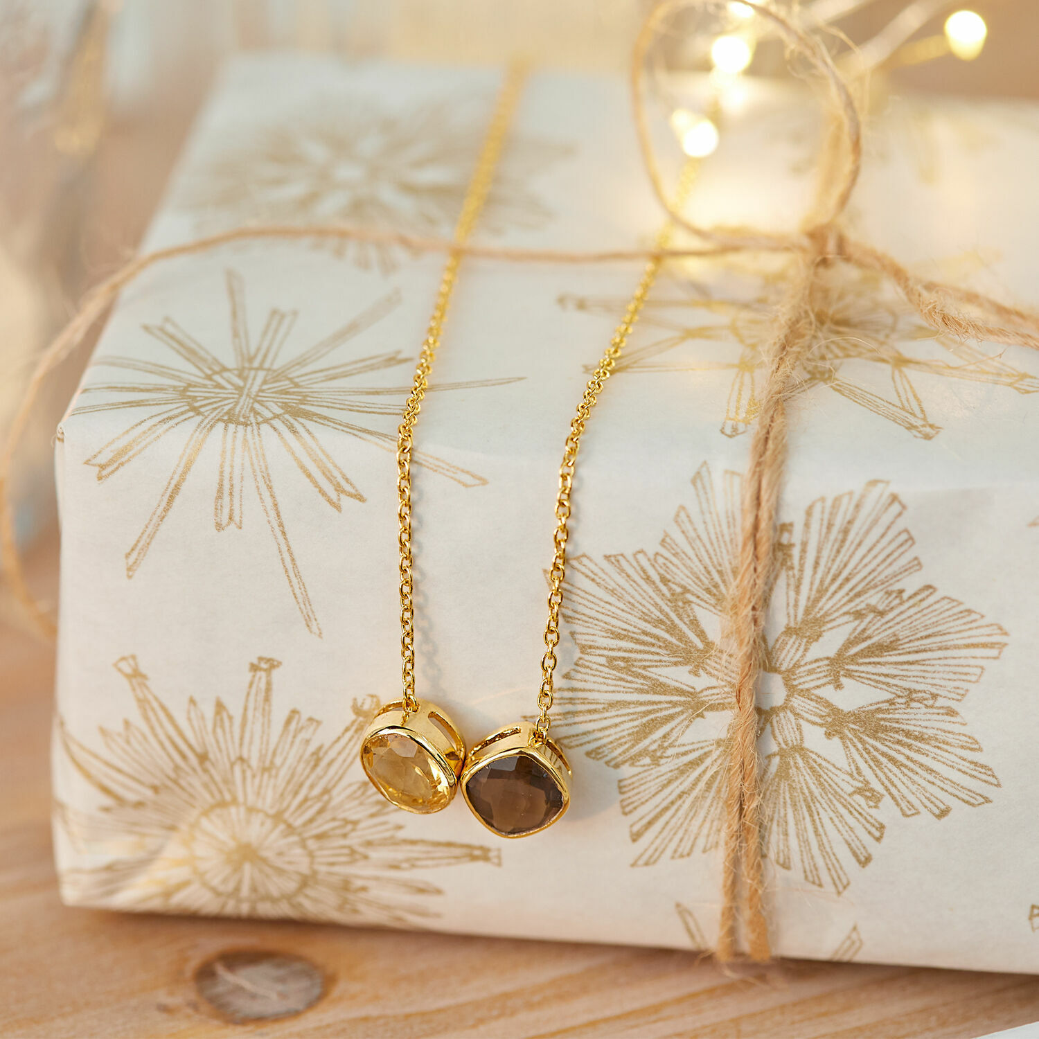 Gouden ketting met twee stenen op een cadeau met decoratief papier en touw