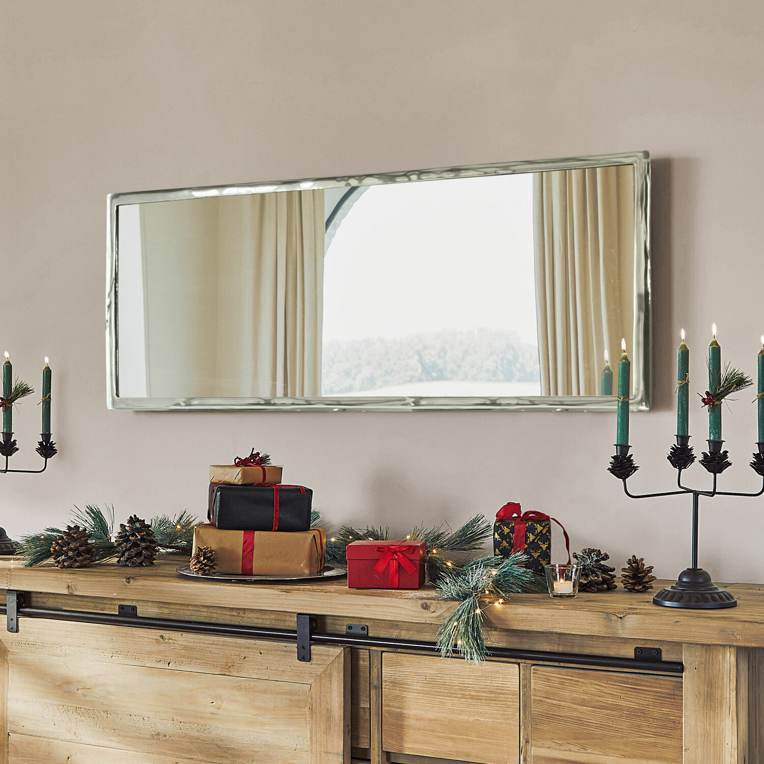 Rechthoekige spiegel met zilverkleurige metalen lijst boven houten dressoir met kerstdecoratie