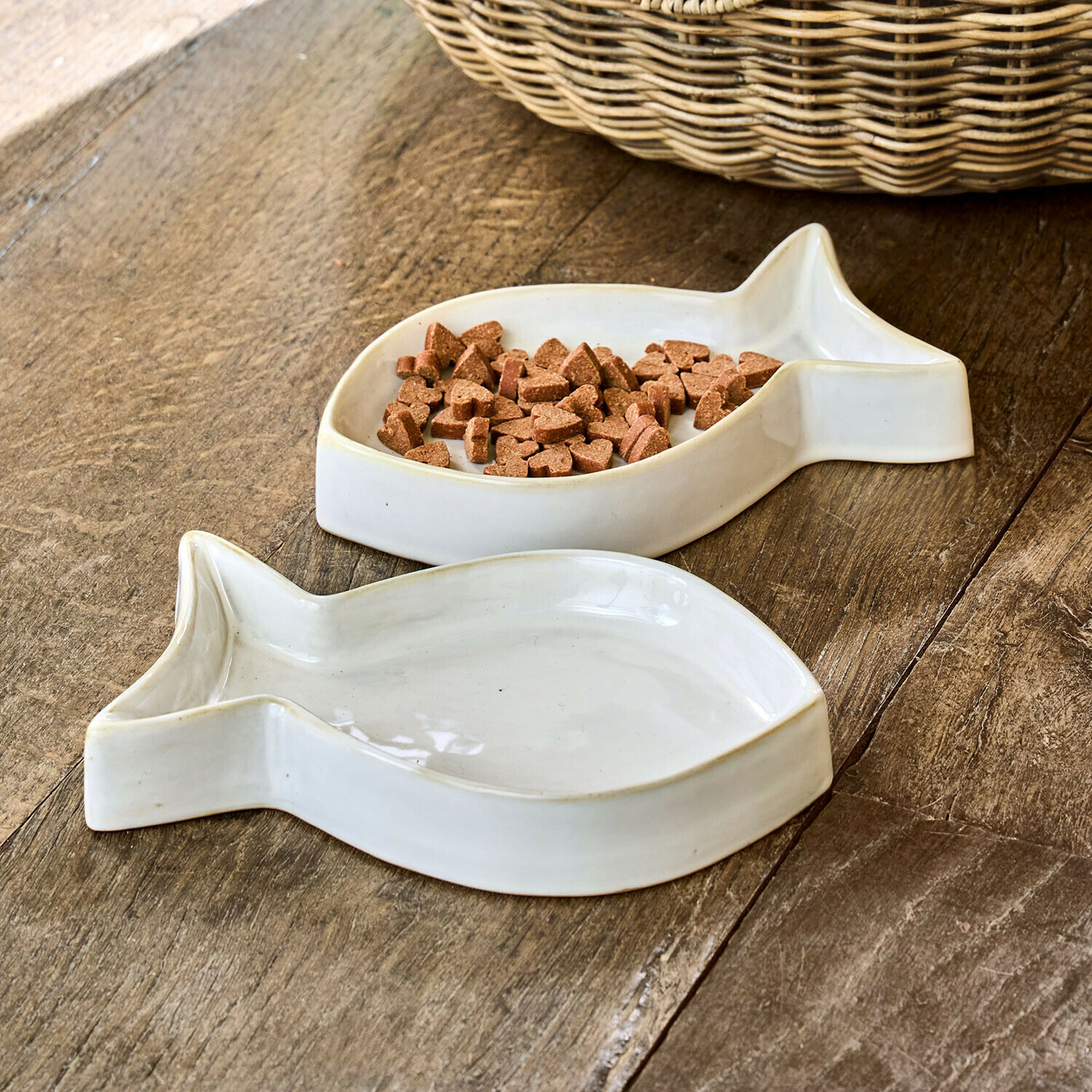 Witte keramische vissenvormige voerbakken met dierenvoer op houten tafel