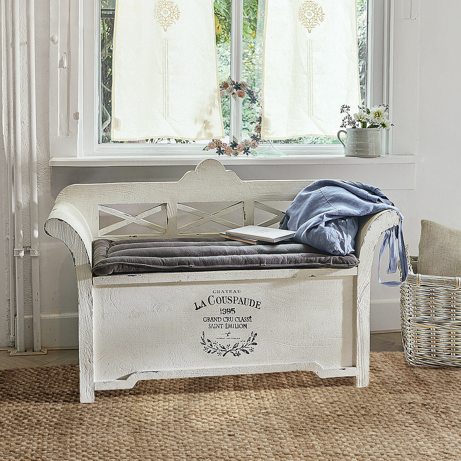 Witte houten bank met zacht kussen en blauwe deken in gezellige kamer met vloerkleed