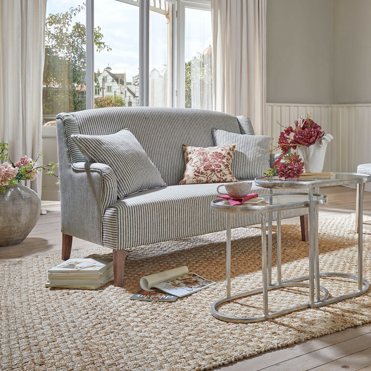 Gestreepte grijze stoffen bank met kussens en metalen salontafels in lichte woonkamer