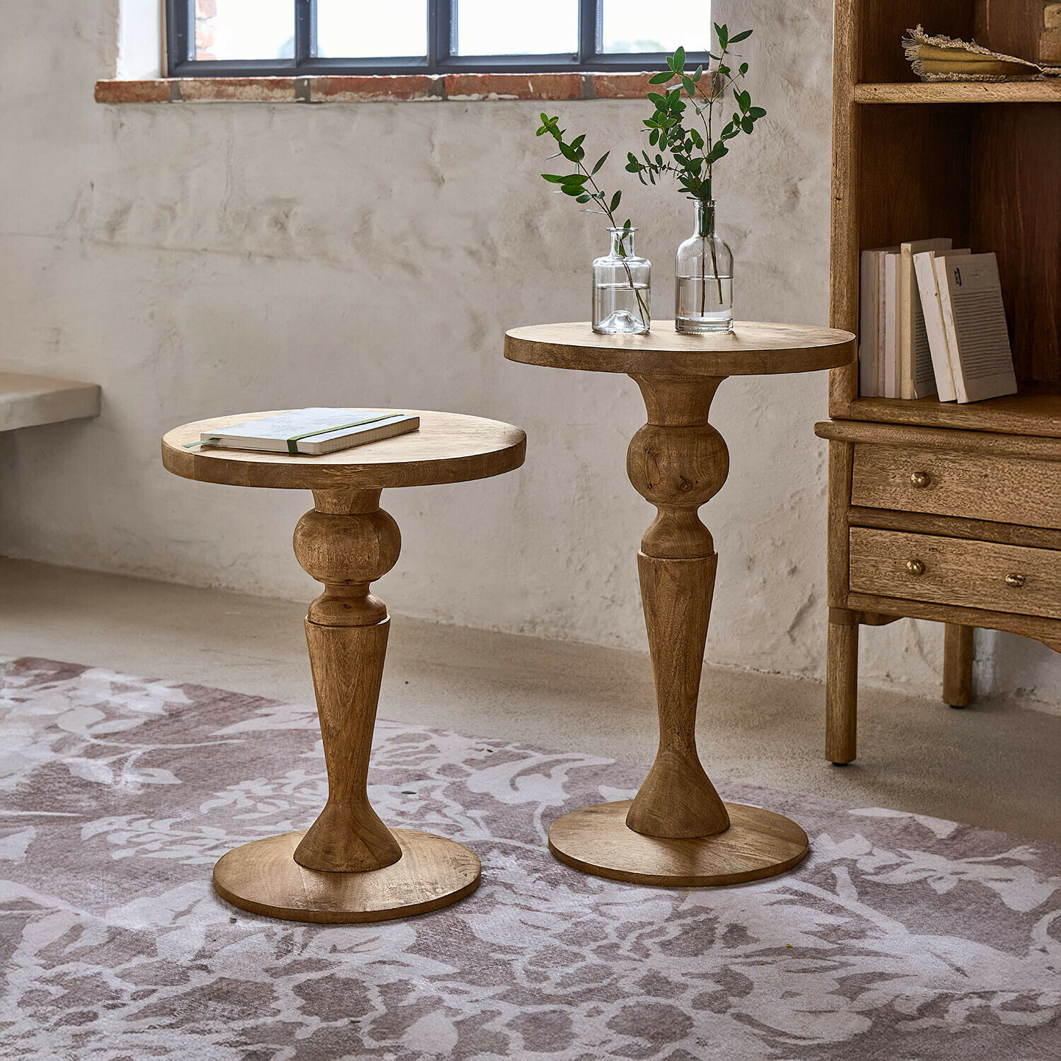 Twee ronde bijzettafels van mangohout in natuurlijke kleur op een vloerkleed met bloemmotief